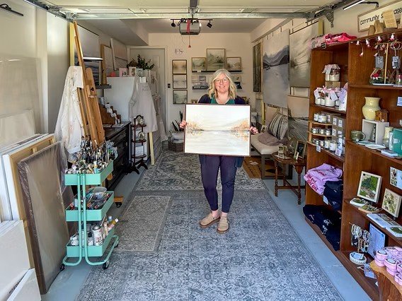 image of Feona holding a landscape painting in her studio