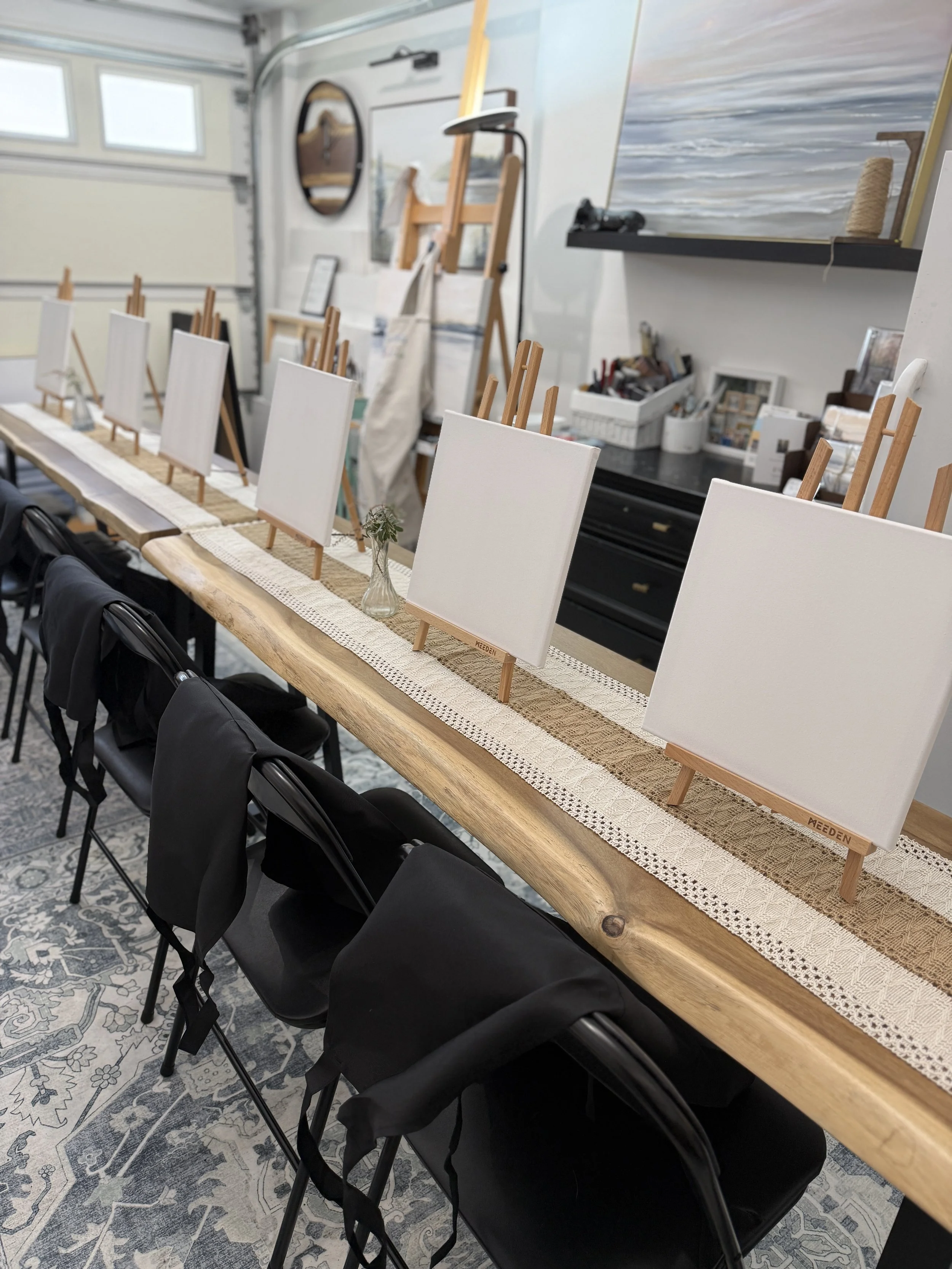 a long table with blank canvases and paint easels in the studio