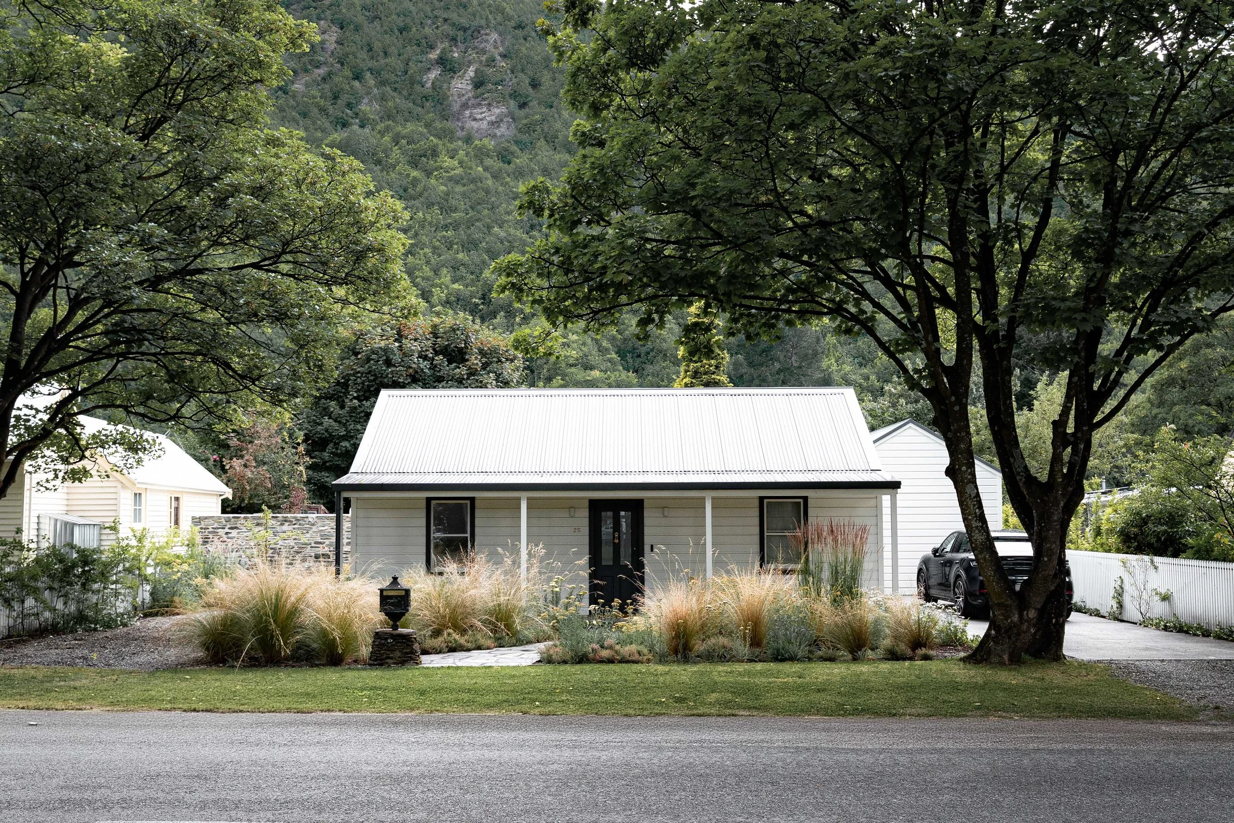Front garden landscape design of a white timber cottage in Arrowtown, featuring a manicured lawn and a textured border of native New Zealand tussock grasses.