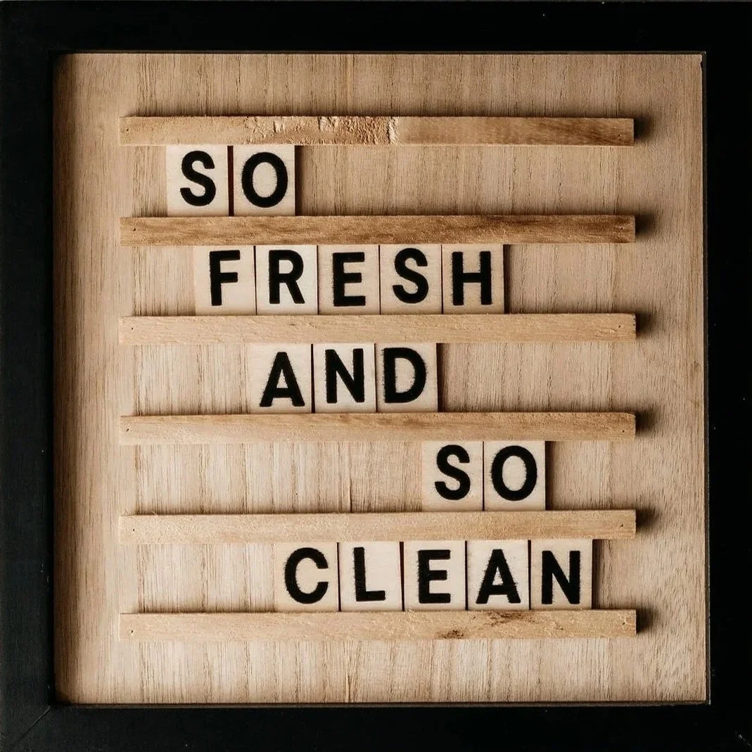 Wooden board with message 'So fresh and so clean' spelled out with black letters on white tiles and some wooden strips.
