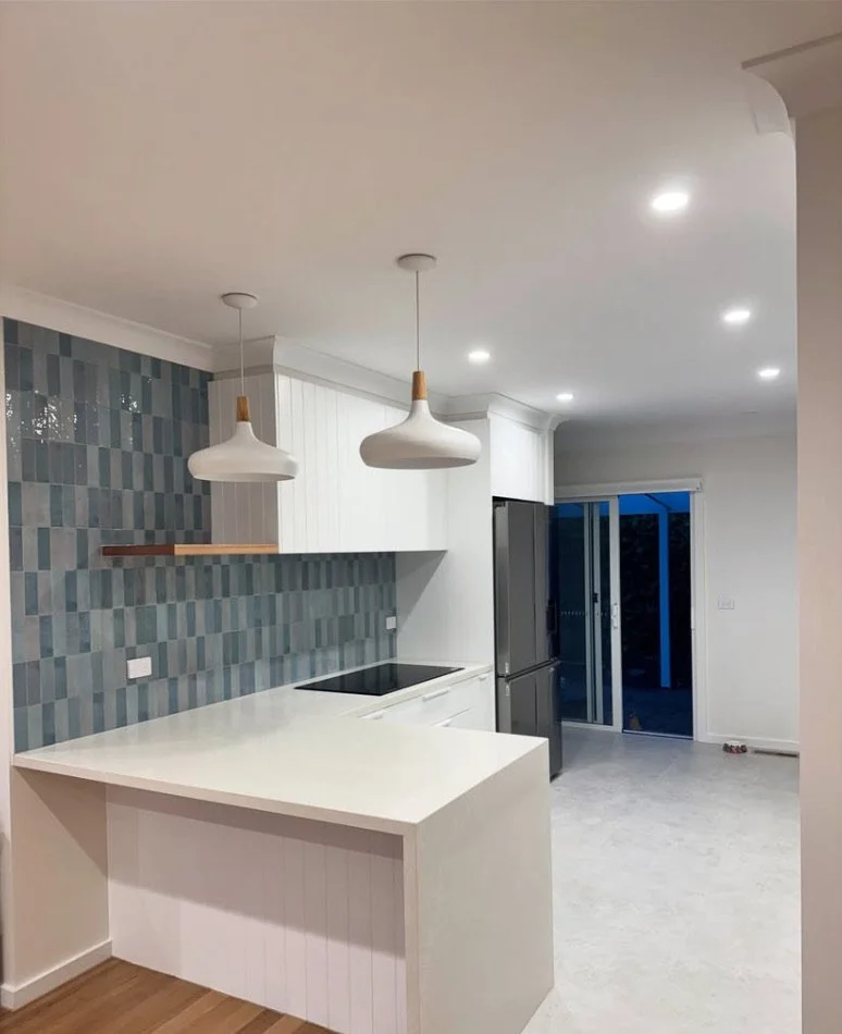 Modern kitchen renovation in Mount Eliza with white countertops, blue and grey tiled backsplash, white cabinets, stainless steel refrigerator and black stove. All flooring, joinery and tiled areas have been caulked and sealed