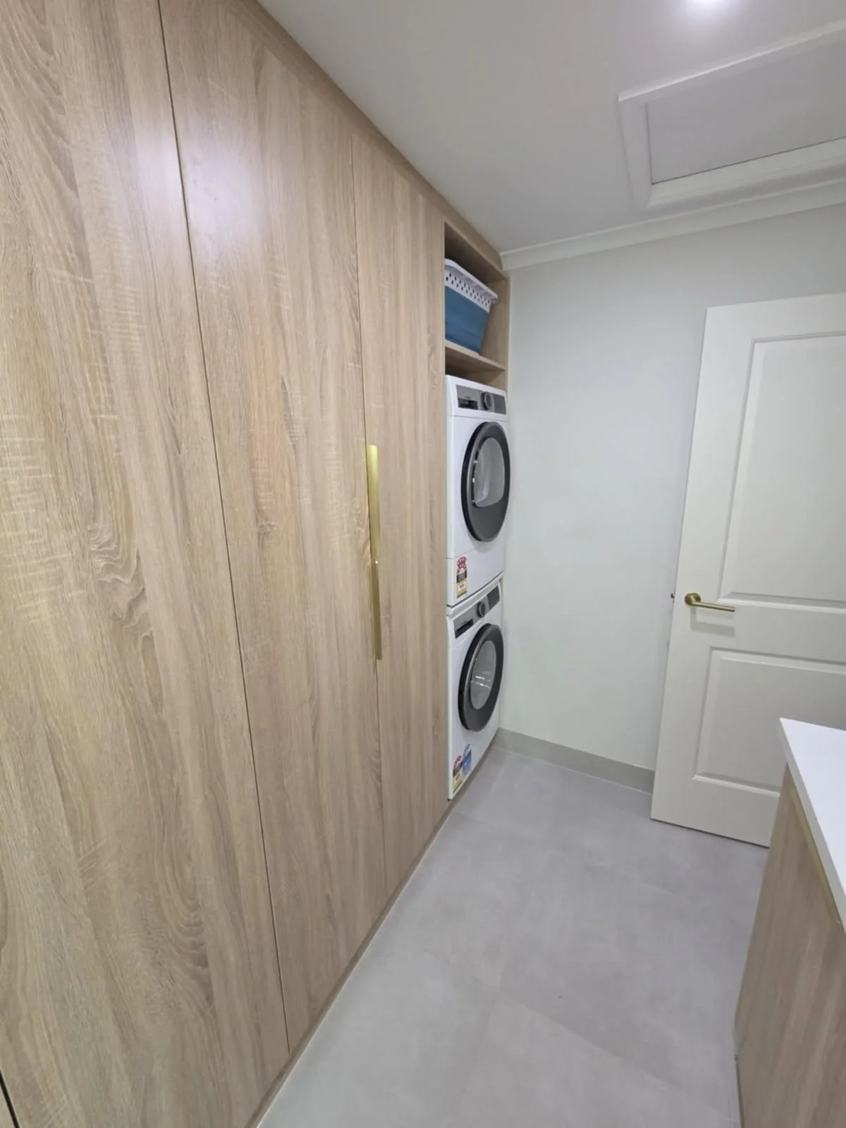 A laundry room that has been renovated in maroondah with a built-in wooden cabinet and a stacked washer and dryer. All joinery and tiled areas have been caulked and sealed by a professional caulker.