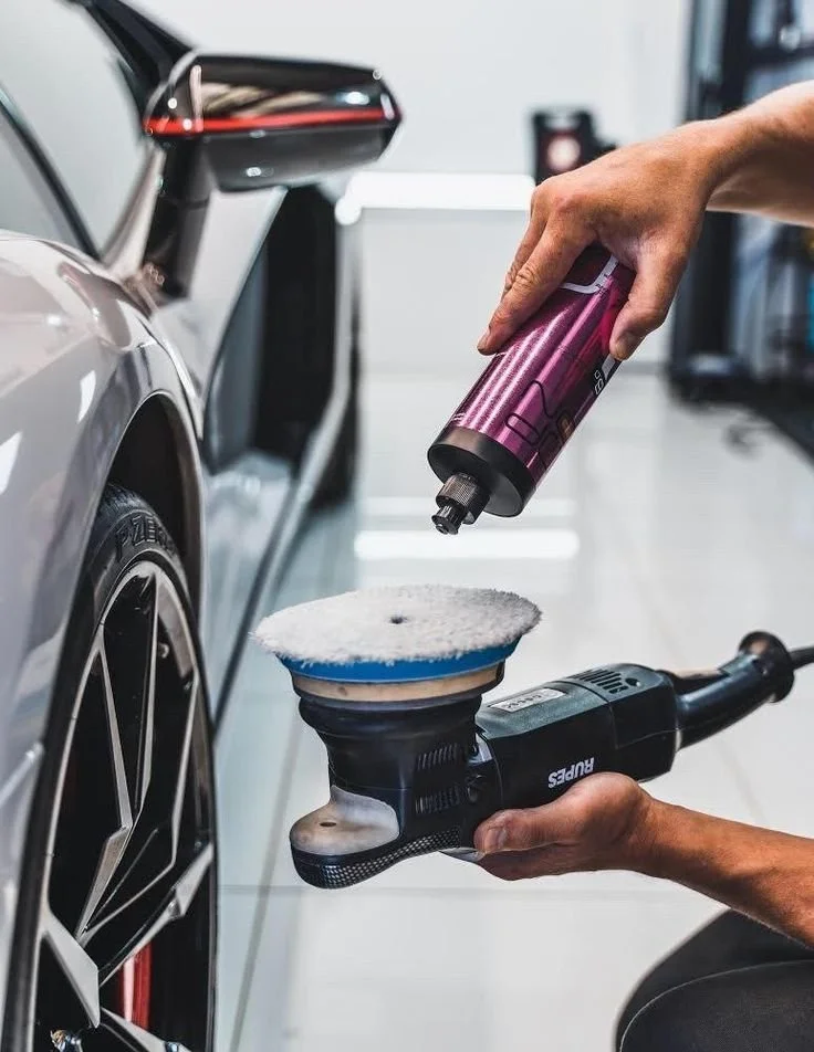 Person cleaning or polishing a silver car with an electric buffer and a foam applicator, focusing on the car's wheel.