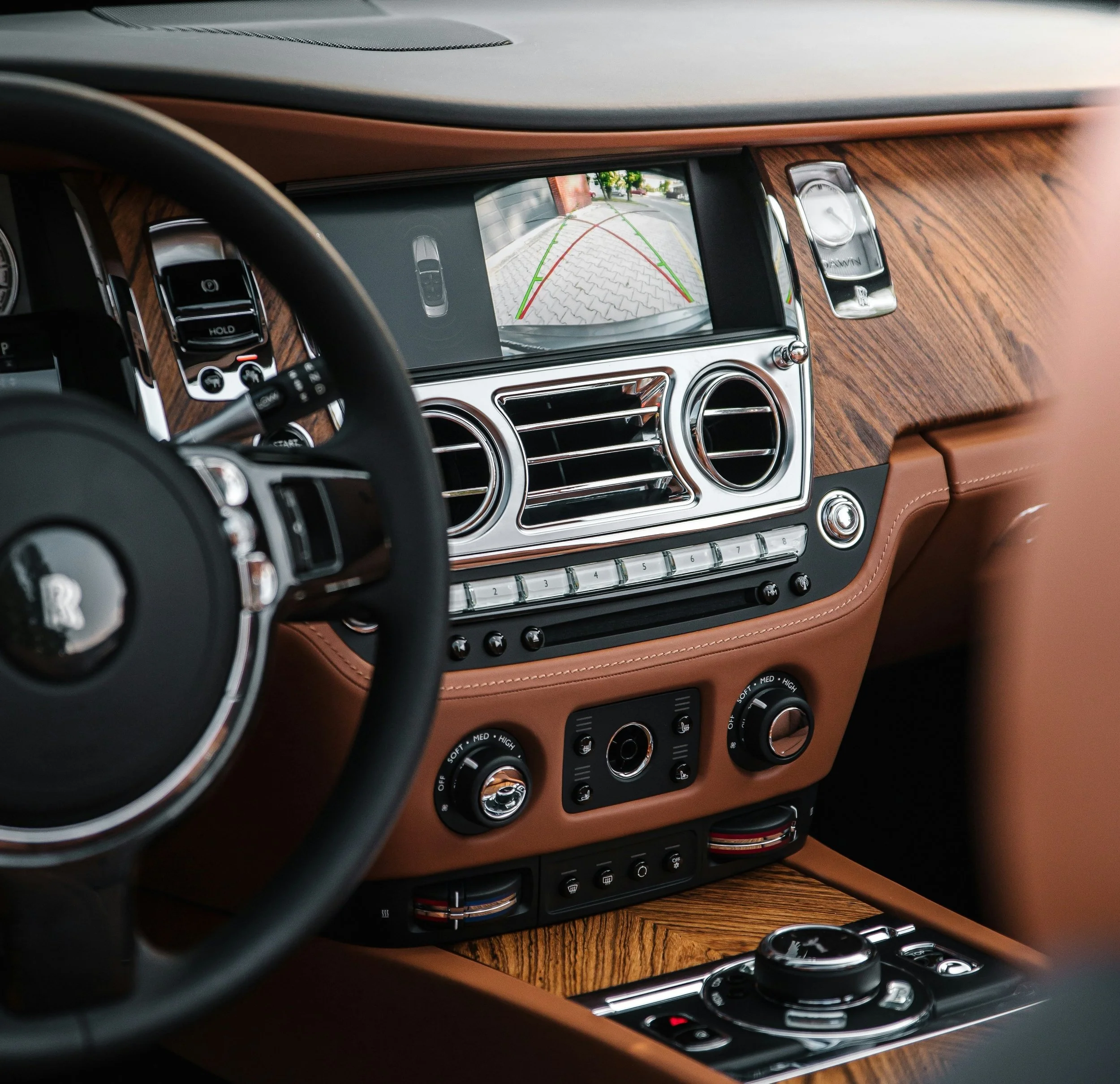 Interior of a luxury car dashboard with a GPS screen showing a rearview camera feed, wood trim, and control buttons.