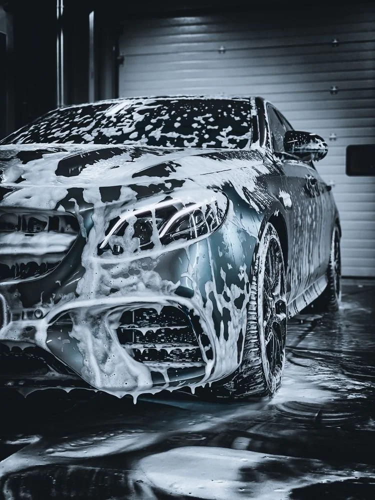 A silver sports car covered in soap suds during a car wash inside a garage