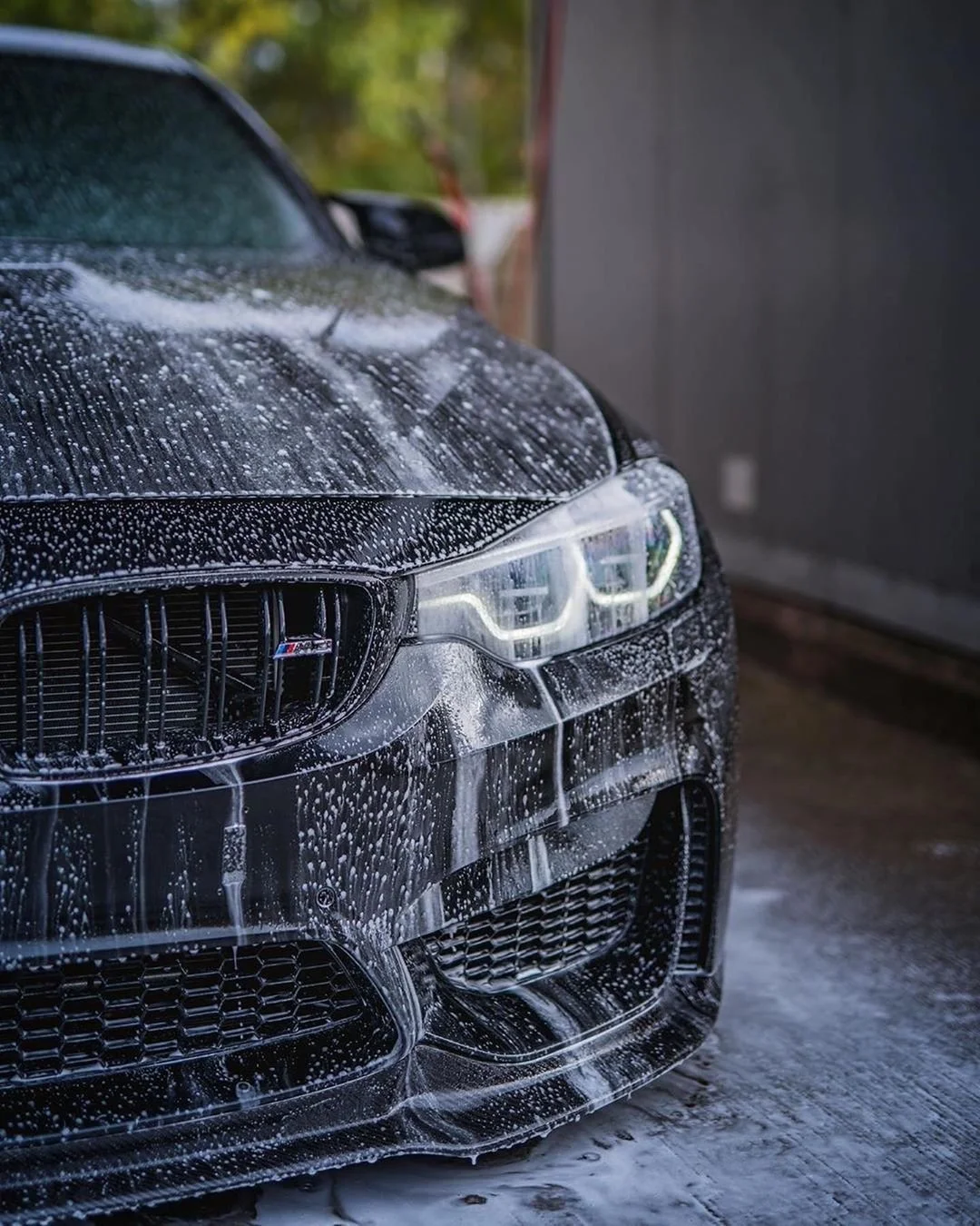 Black sports car being washed with soap and water, soap suds covering the front part, including the grille and headlights.