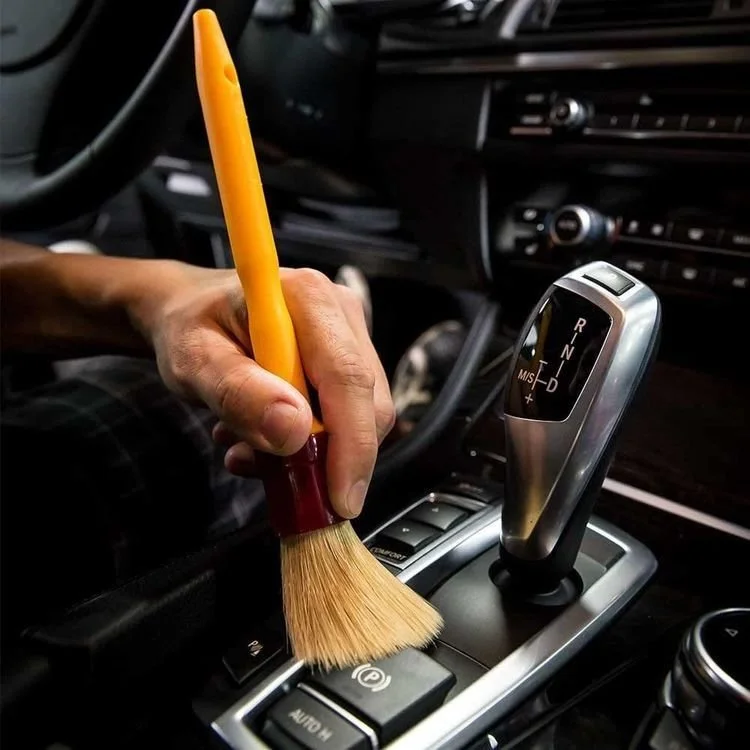 Person cleaning the gear shift of a car with a small cleaning brush.