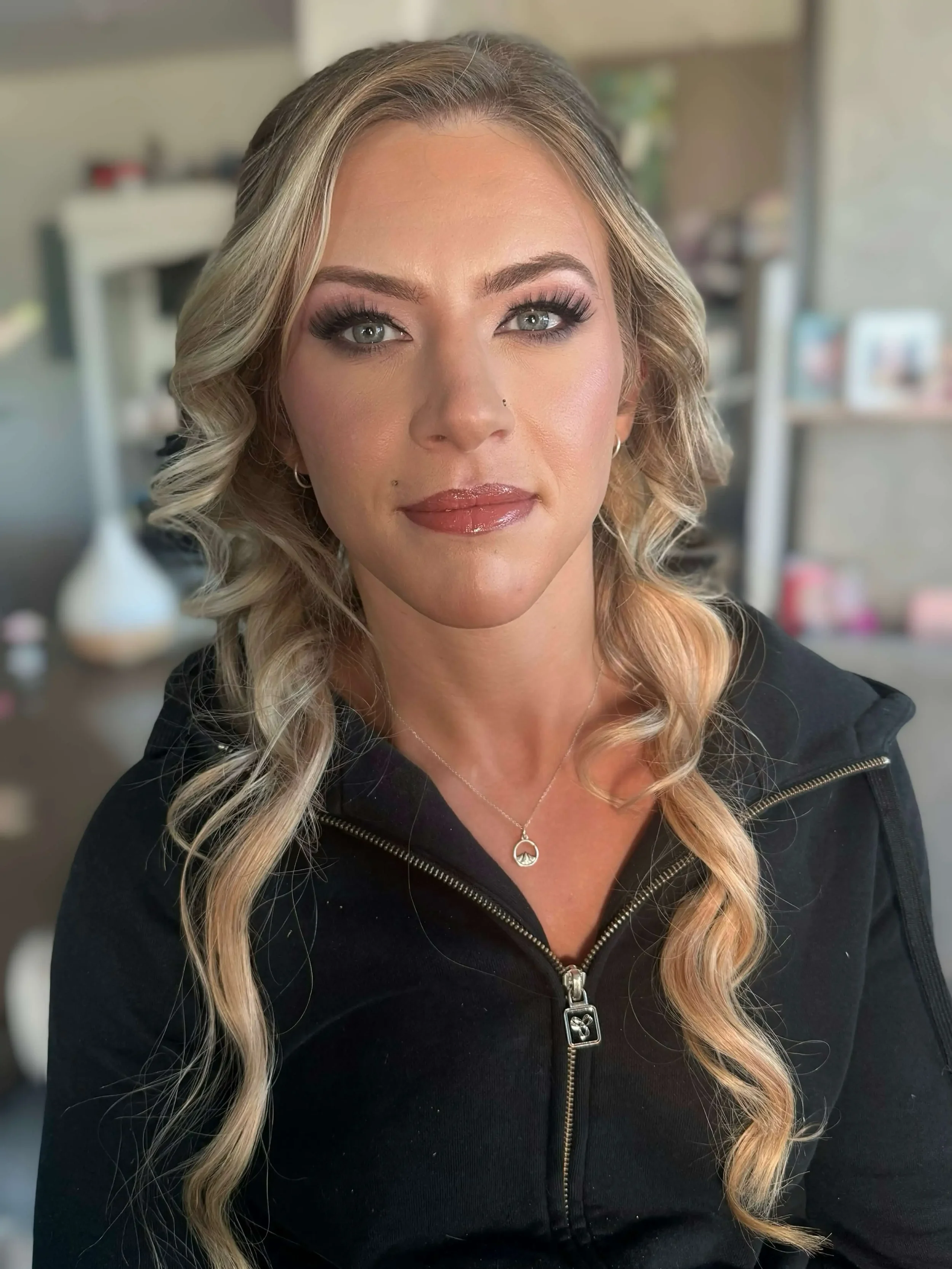 She has smooth, natural-looking skin, defined brows, dramatic lashes, soft mauve eyeshadow, and a glossy rose-brown lip for an elegant, polished look