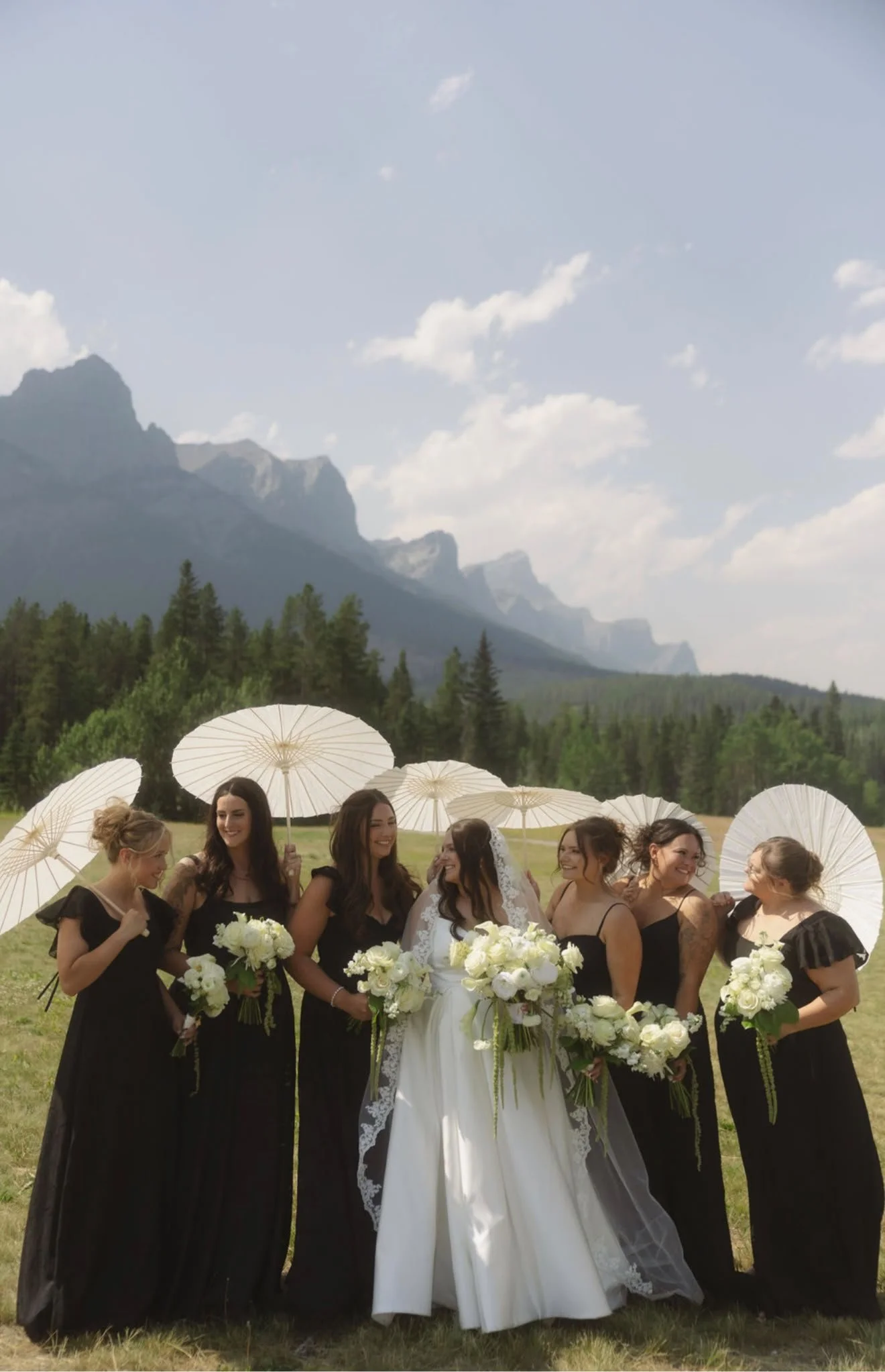 Bride and bridesmaids with parasols and white bouquets in the Rocky Mountains, hair and makeup by North of Blush