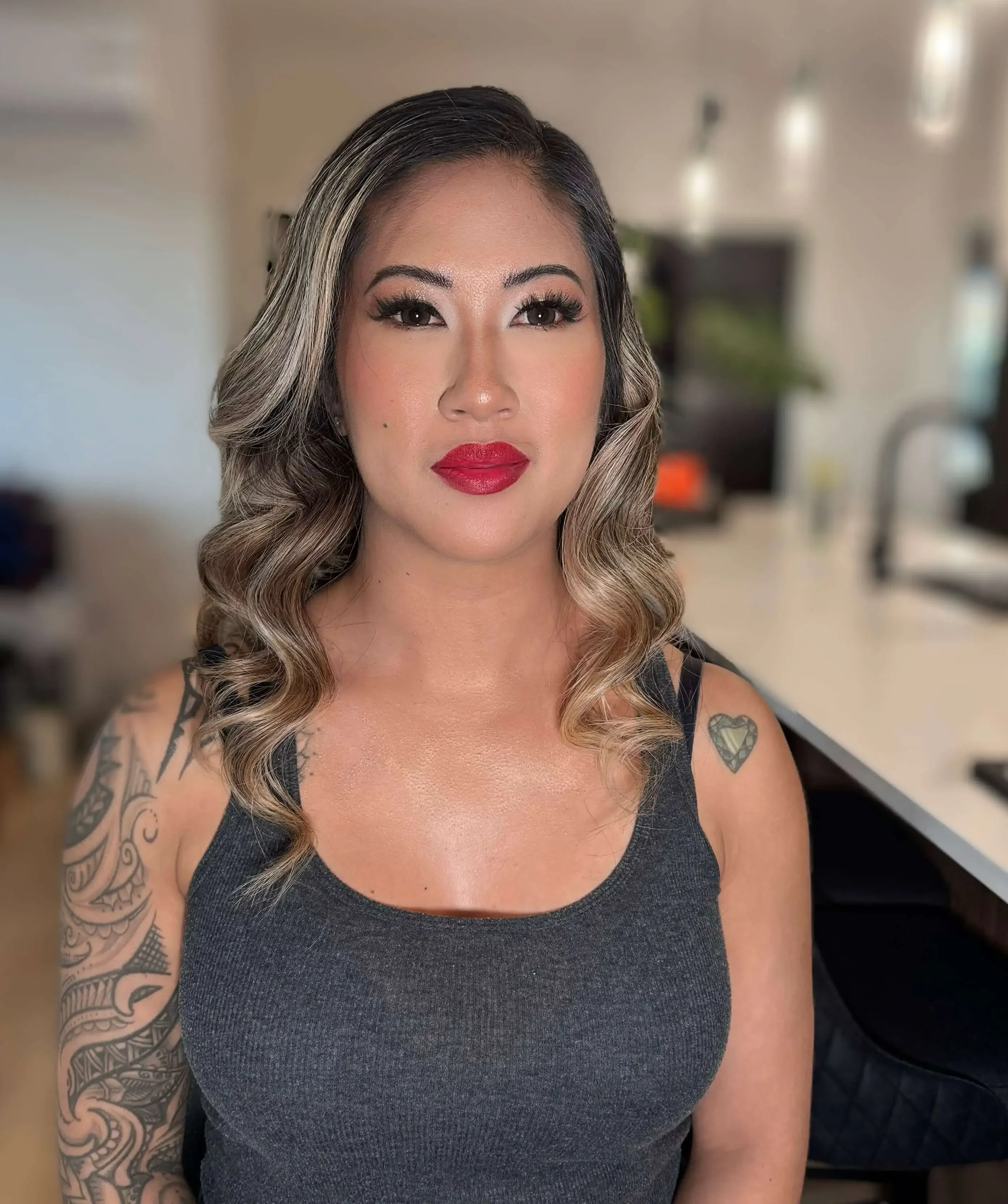 Full glam makeup with soft neutral eyeshadow, bold lashes, warm blush, glowing skin, and classic red lipstick.
