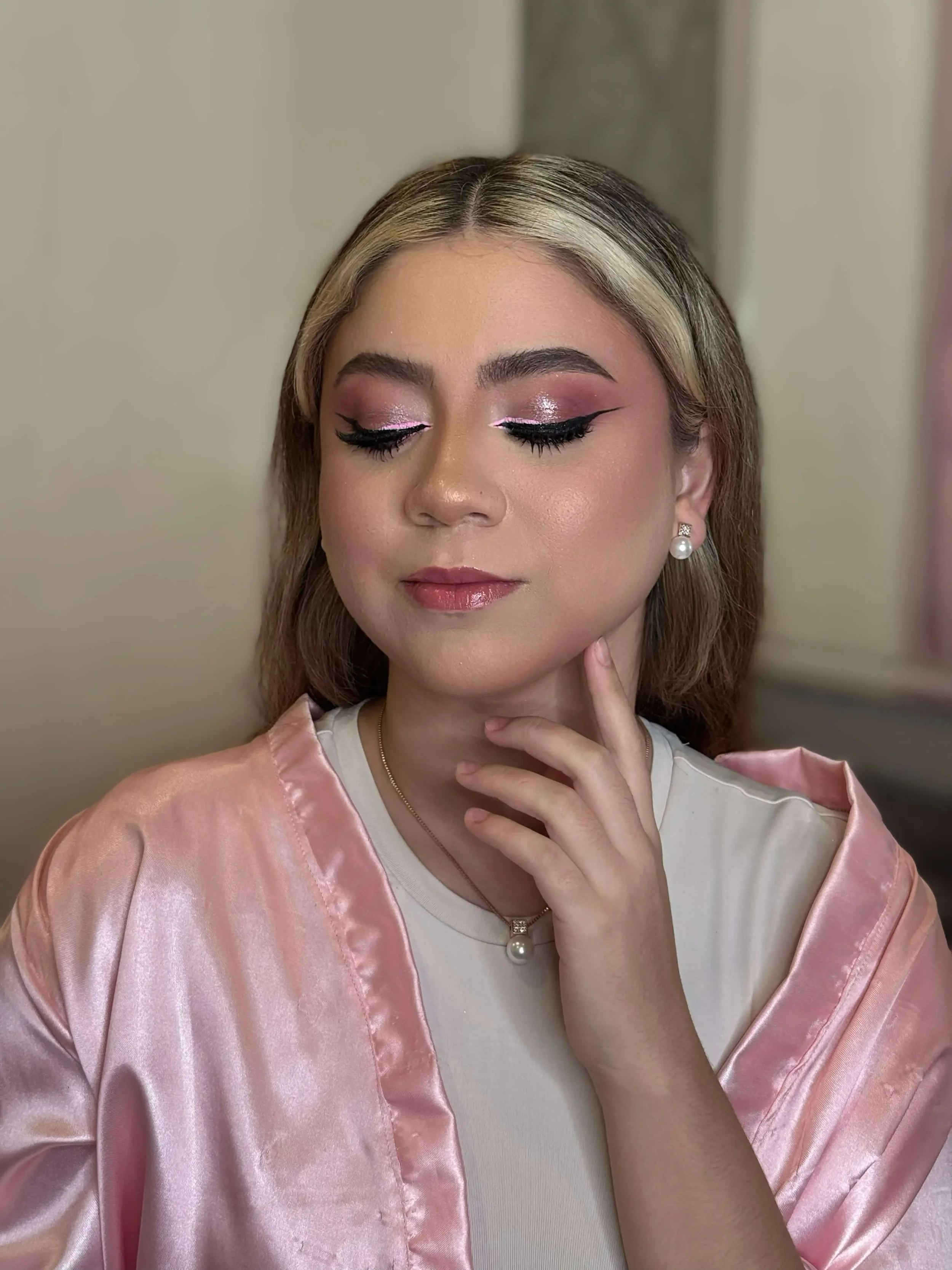 Soft glam makeup with pink shimmer eyeshadow, winged eyeliner, long lashes, glowing skin, and natural rosy lips.
