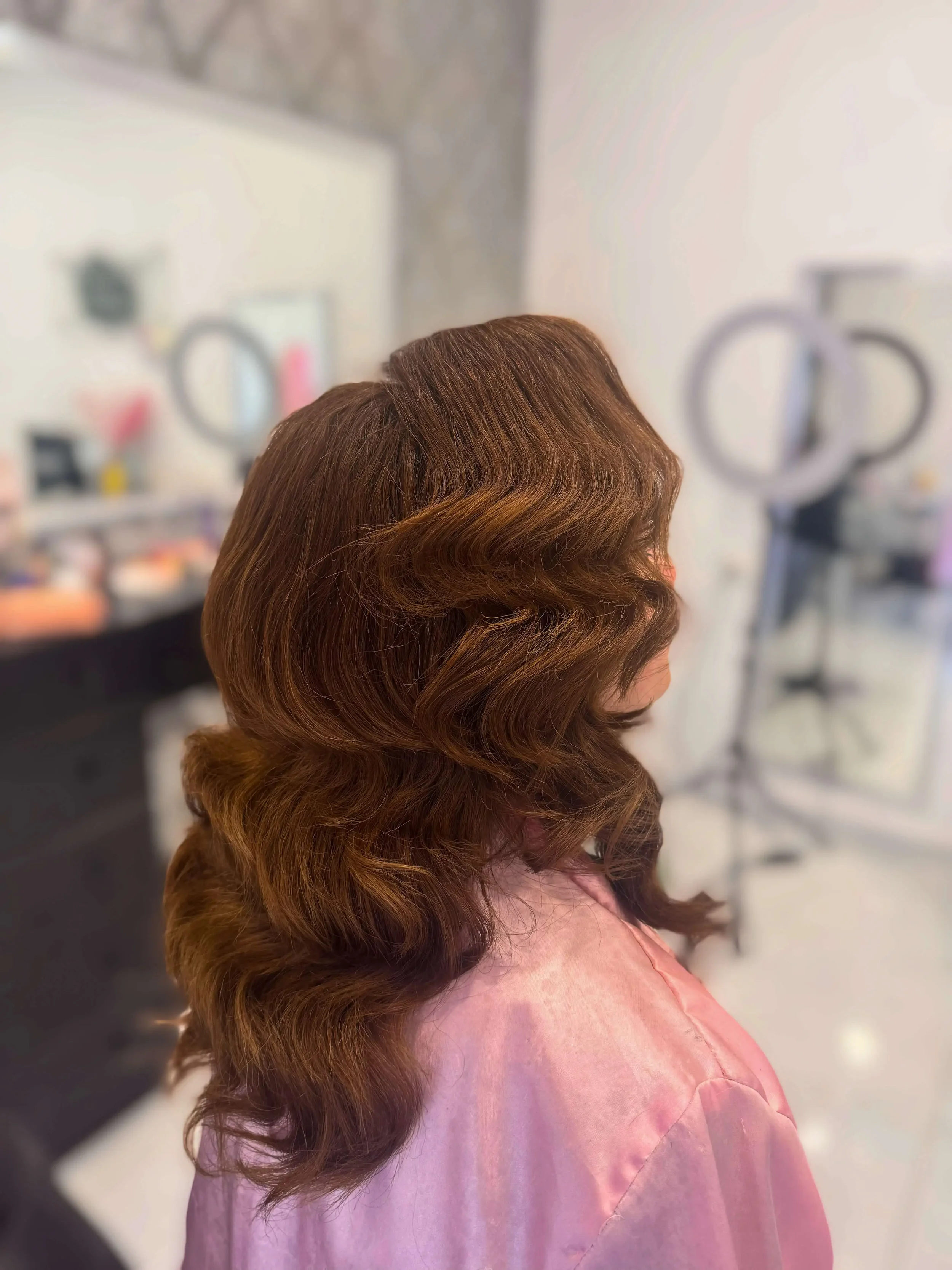 Medium-length auburn hair styled in soft, vintage-inspired waves with smooth volume and shine.