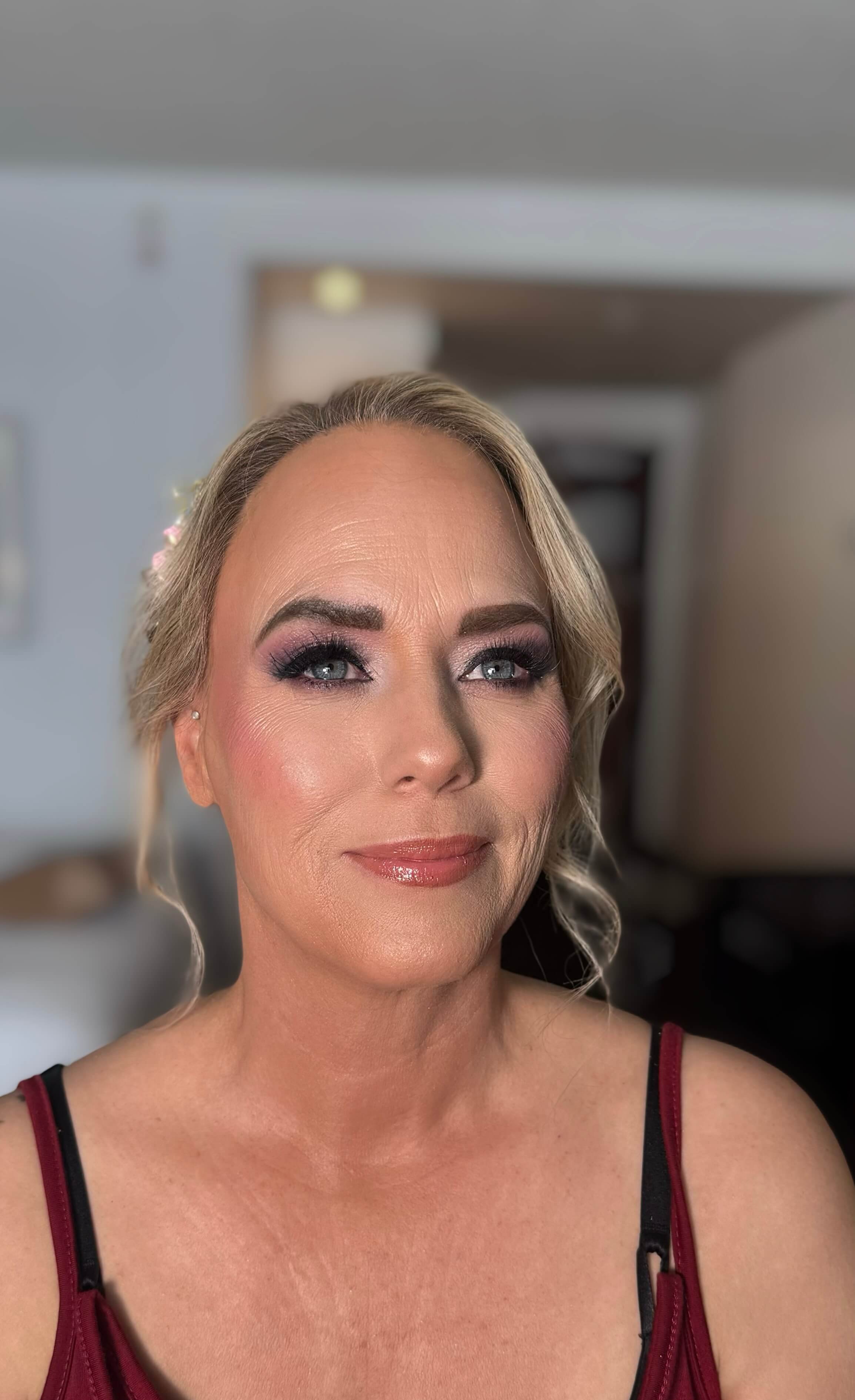 Soft glam makeup with smooth, even skin, defined brows, smoky eye makeup with long lashes, rosy blush, and glossy nude-pink lips.