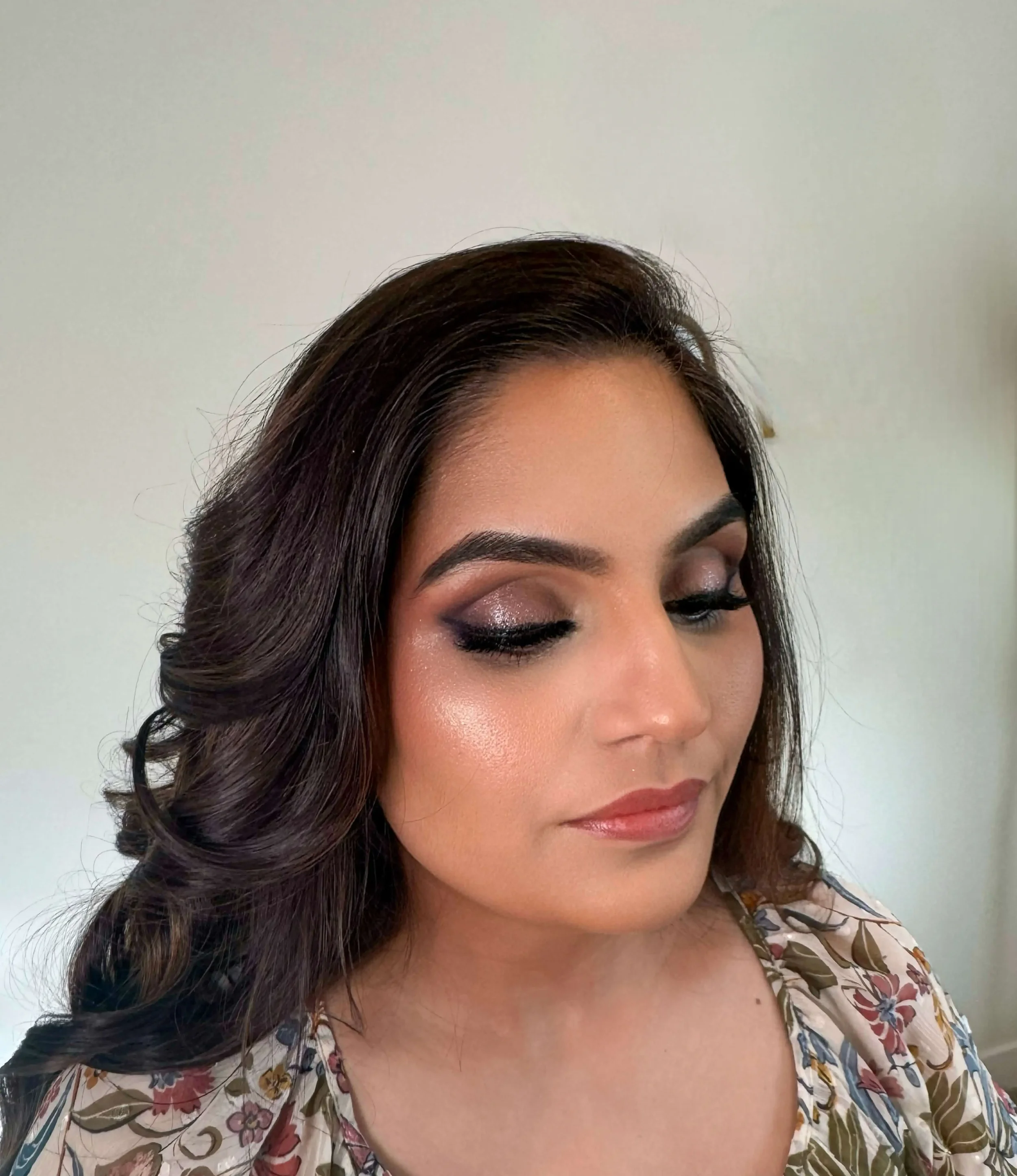 She wears glowy skin, bold defined brows, shimmery smoky eyes with long lashes, and a soft rose-nude lipstick for a glamorous finish.