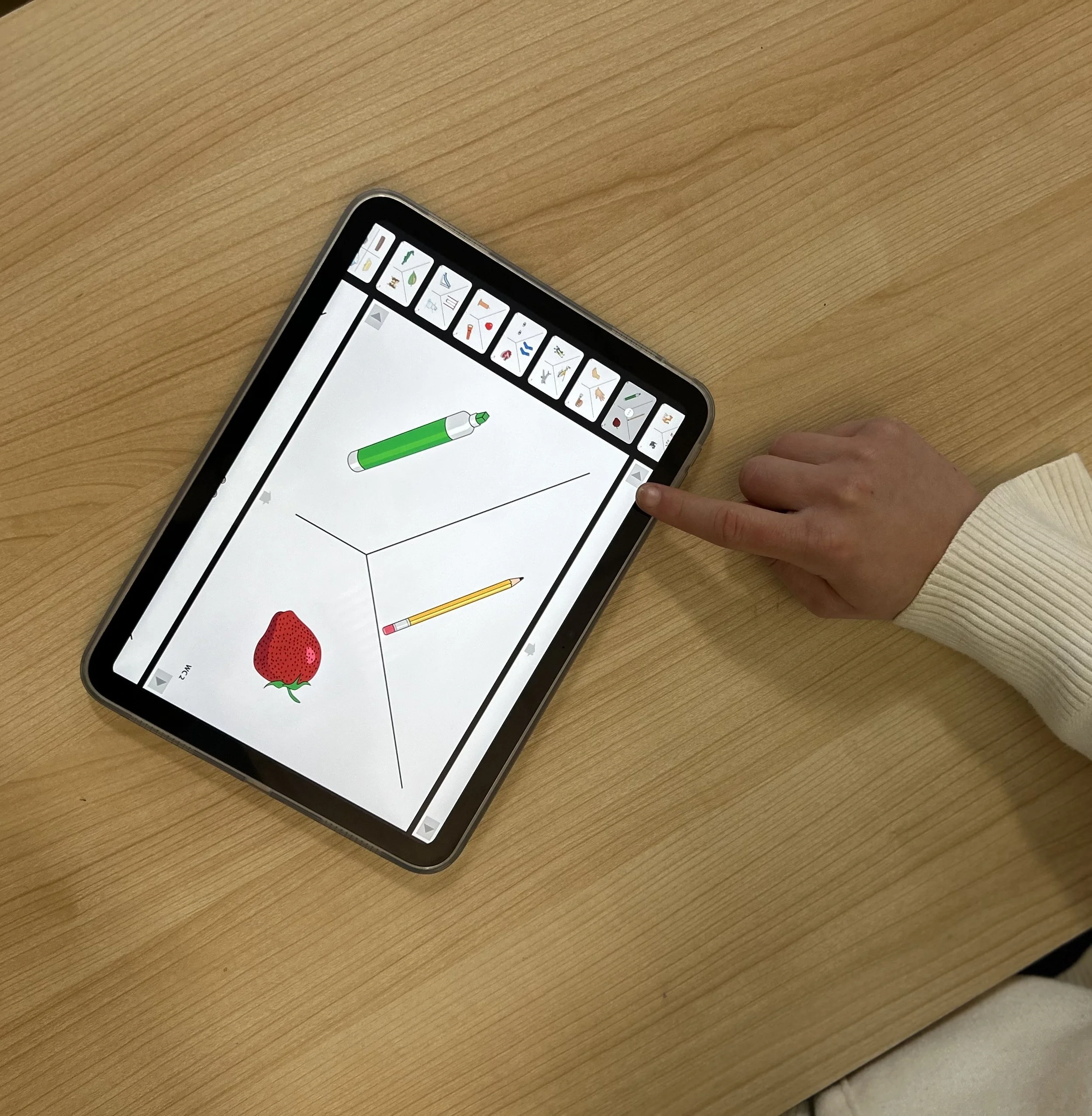 A person using a tablet with a drawing application, drawing a 3D cube with a strawberry, a green marker, and a yellow pencil on the workspace.