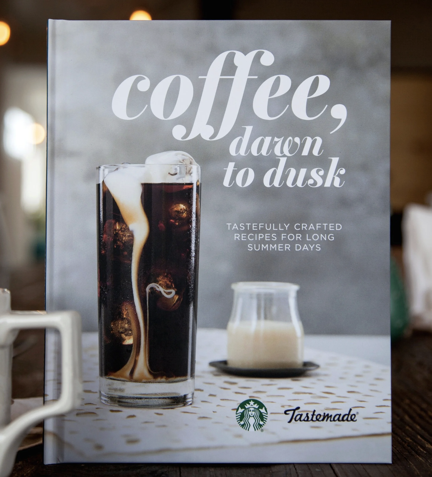 A menu cover with a photograph of iced coffee with cream being poured into it. Text on the cover reads 'coffee, dawn to dusk.' The logo of Starbucks is visible at the bottom, along with the word 'Tastemade.'