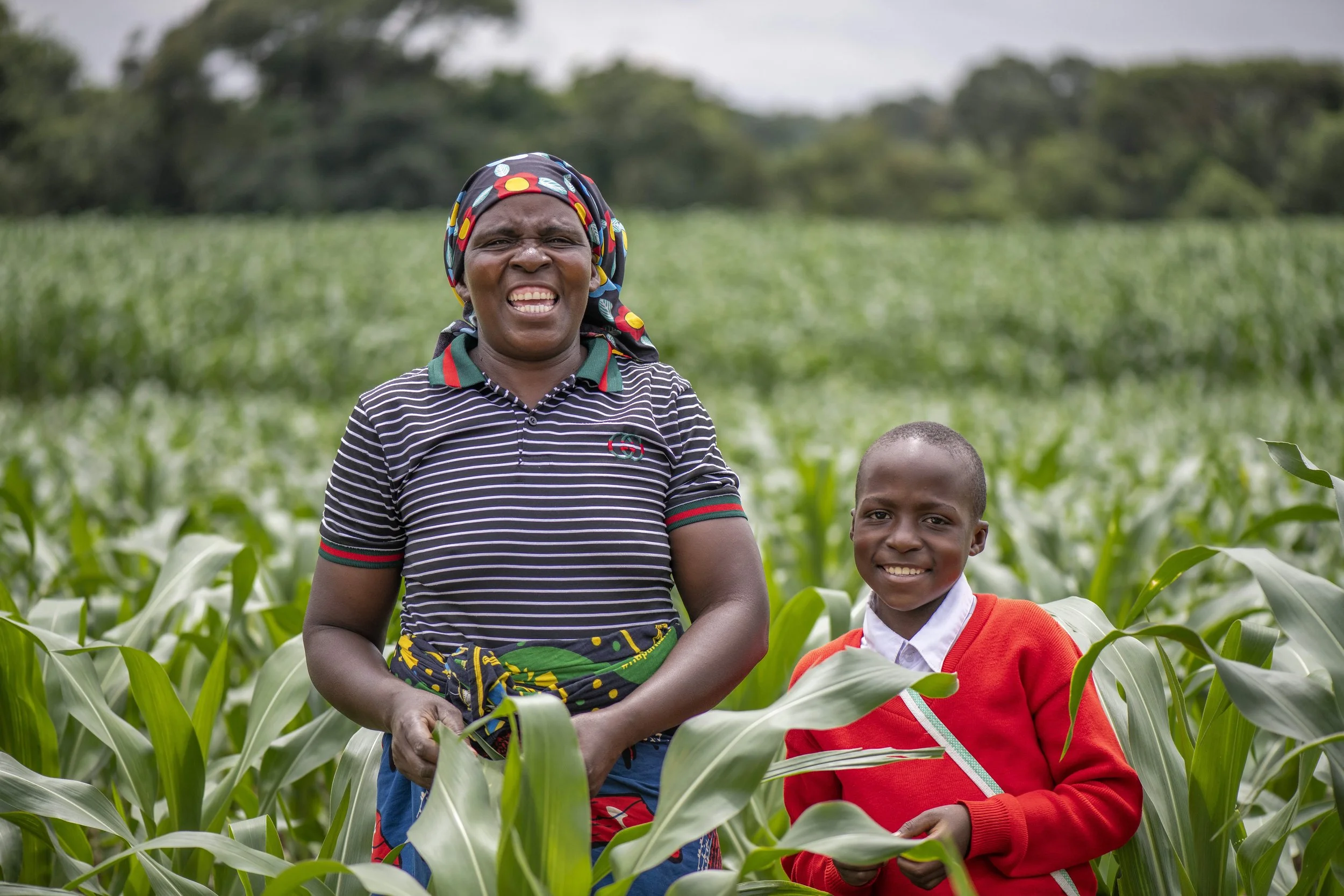 A woman and a boy standing in a green field of crops, smiling and facing the camera.