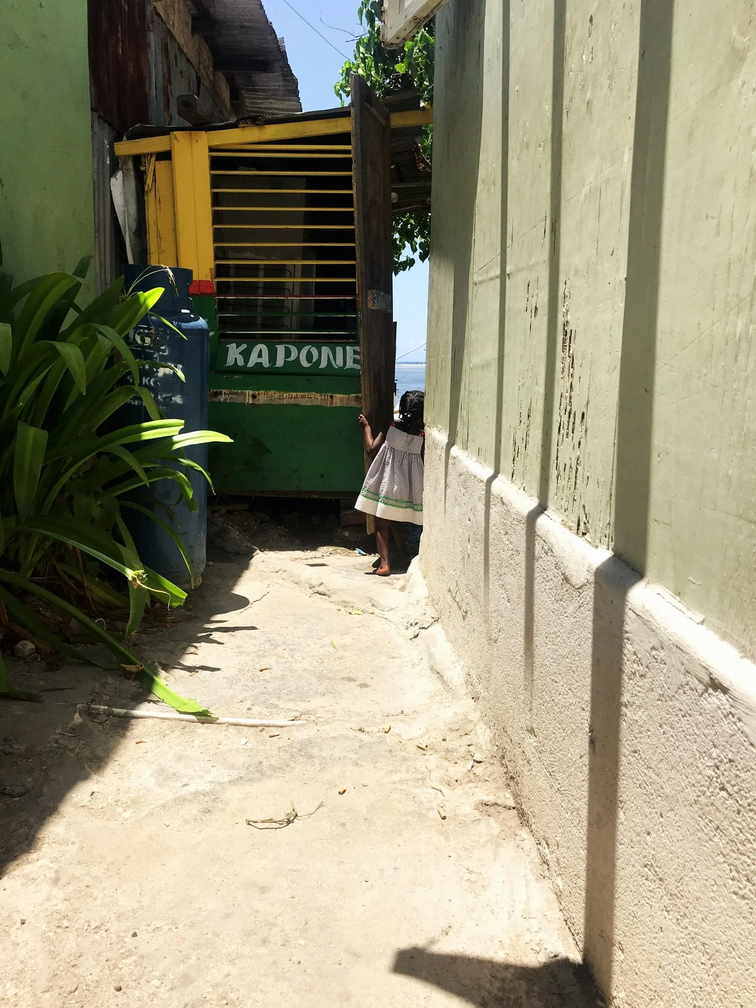 Tucked between worn walls and midday light, a young girl pauses on the threshold of stories untold.