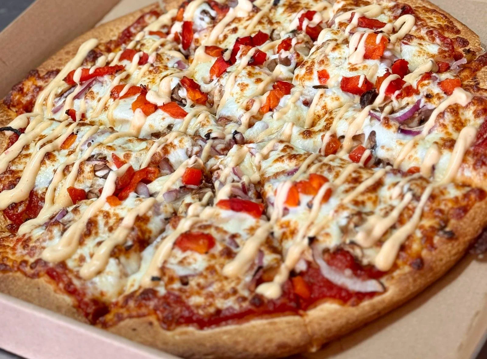Jessie's Pizza Close-up of a large pizza topped with cheese, diced red bell peppers, chopped onions, drizzled with a creamy sauce, in a cardboard box. best pizza in Point Cook