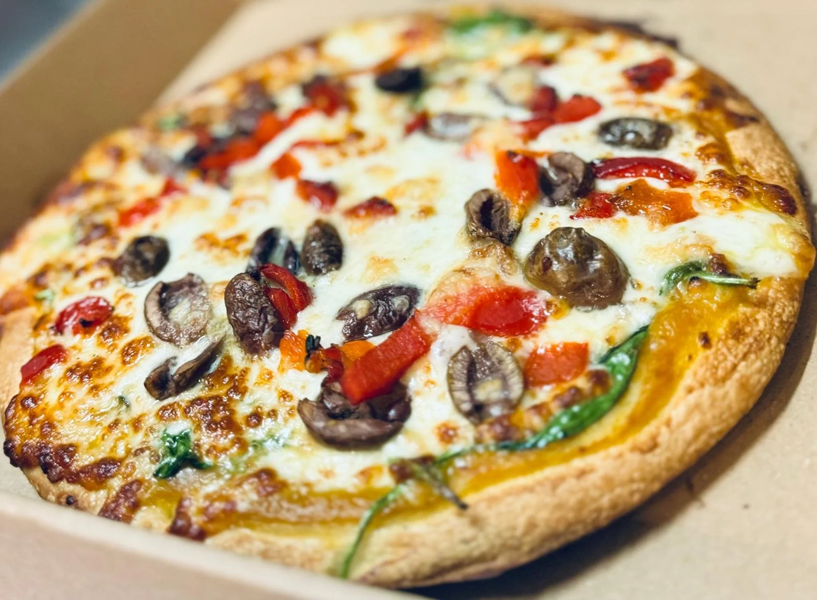 Jessie's Pizza Close-up of a freshly baked pizza with cheese, black olives, red and green peppers in a cardboard box. best pizza in Point Cook