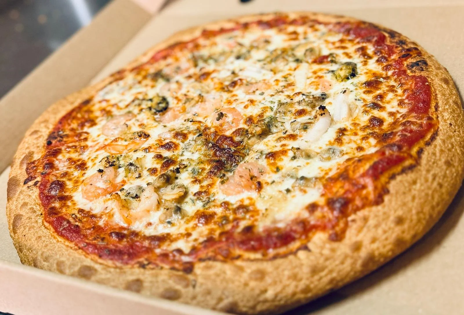 Jessie's Pizza Close-up of a shrimp and seafood pizza with cheese, herbs, and tomato sauce in a cardboard box. best pizza in Point Cook