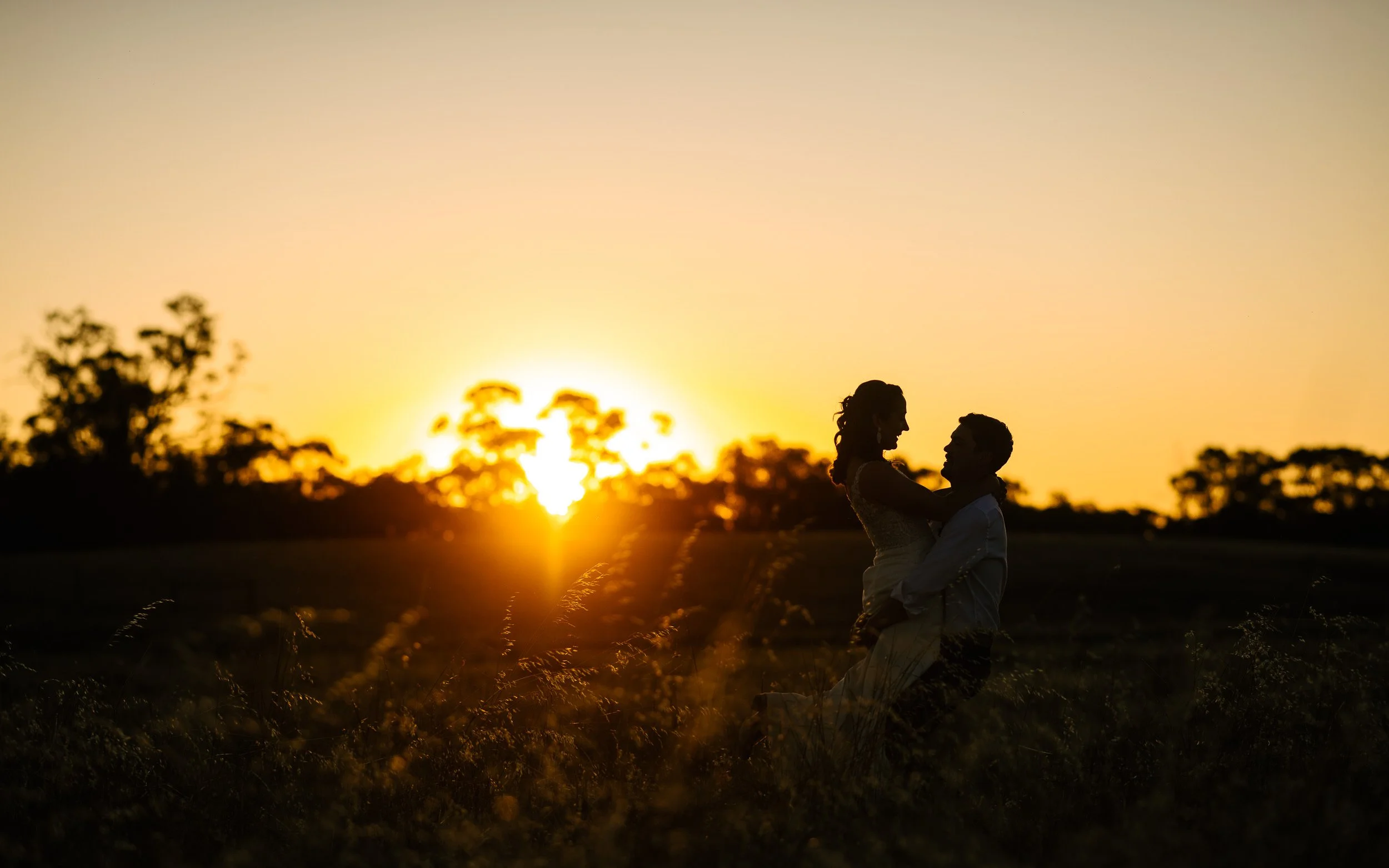 Silhouetted couple at sunset, with the sun low on the horizon and trees in the background.
