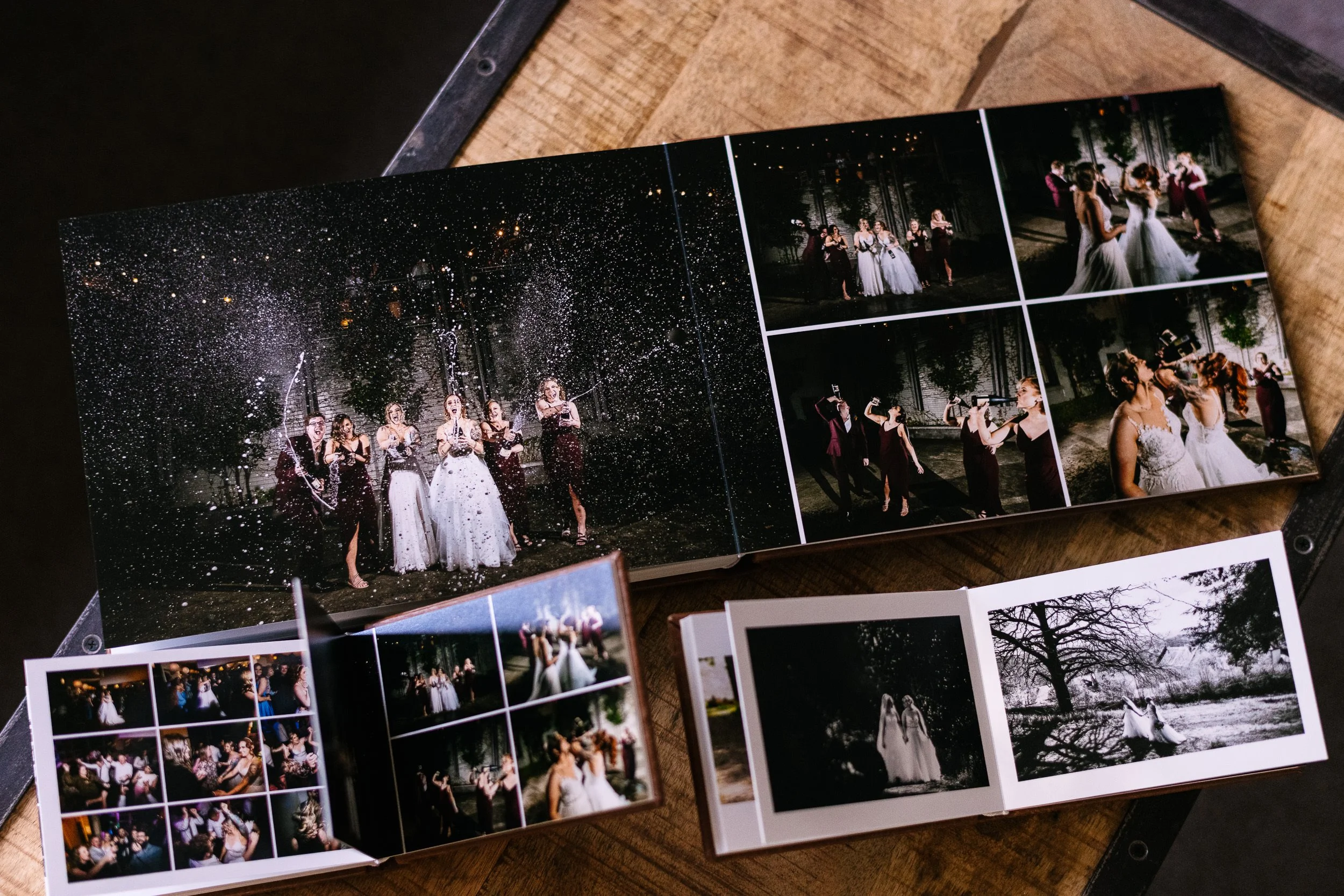 Multiple photo albums open on a wooden surface displaying wedding photos, including group shots with bridesmaids, groomsmen, and couples, with some images taken outdoors at night.