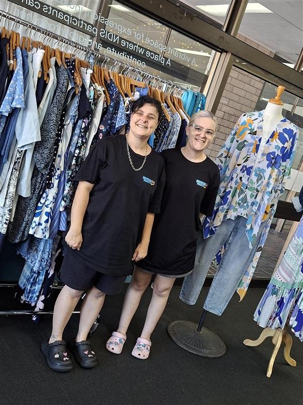 Two participants inside The Oaks Collective secondhand store, standing near clothing racks.