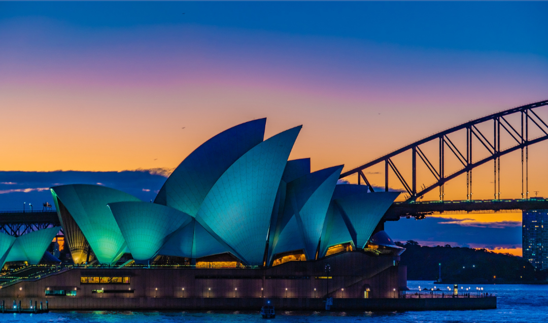 Sydney Opera House illuminated at sunset with Harbour Bridge in background.