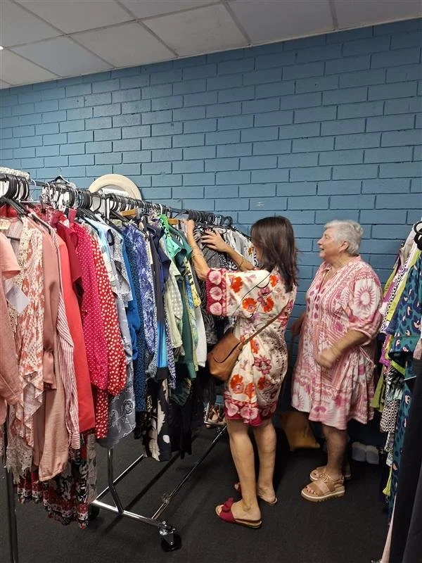Two women shopping and looking at colorful dresses hanging on a clothing rack in a thrift store or clothing shop