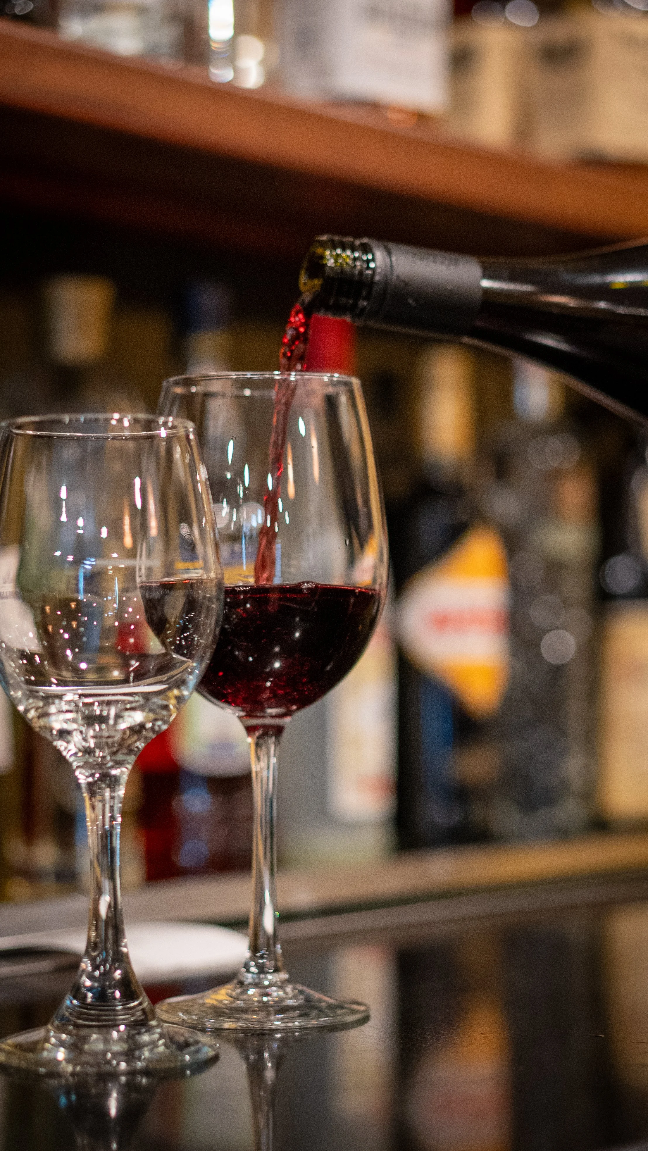Close-up of two wine glasses with red wine being poured into one of the glasses.