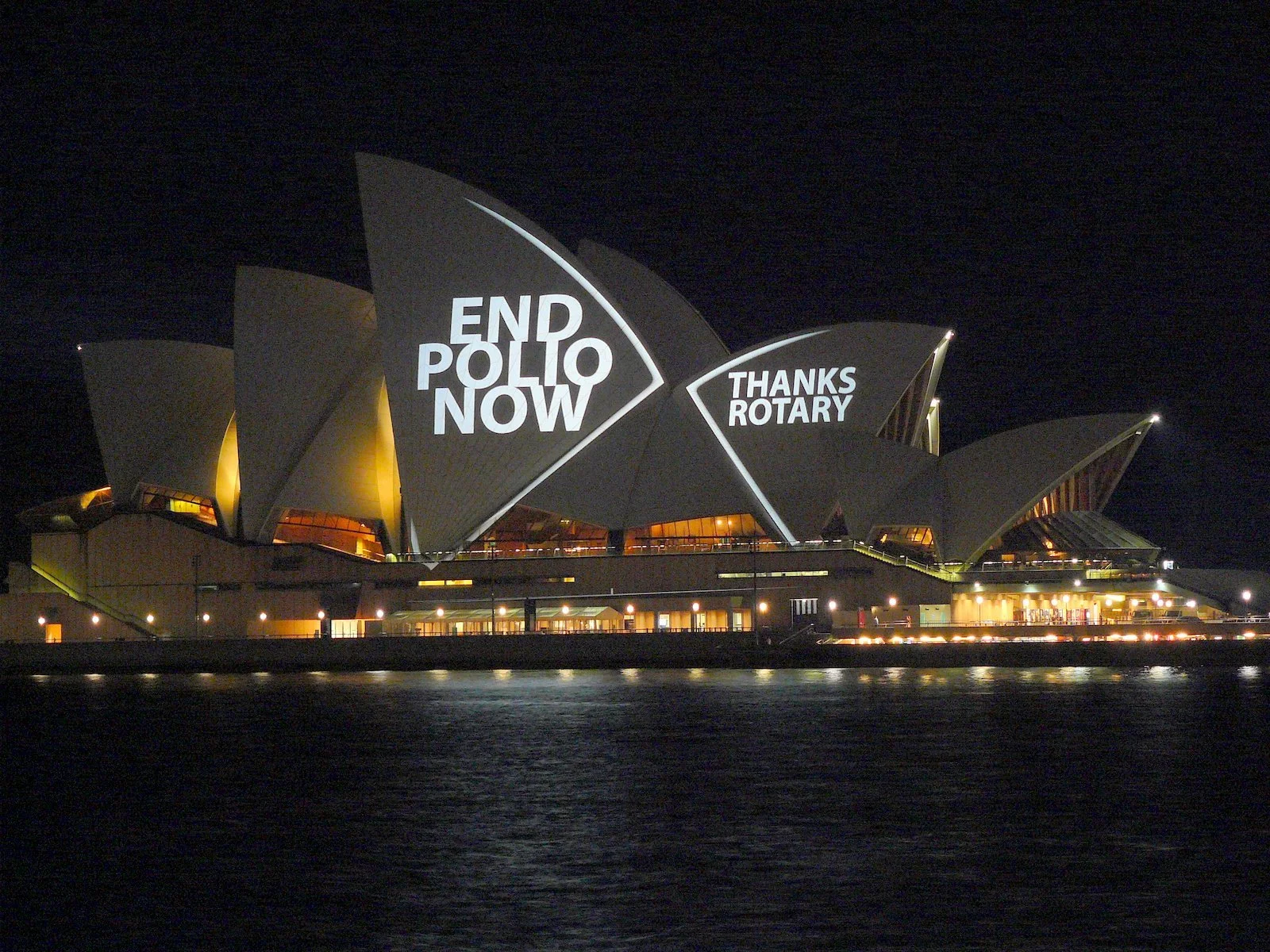 Night view of the Sydney Opera House illuminated with signs reading 'End Polio Now' and 'Thanks Rotary' projected on its sails.