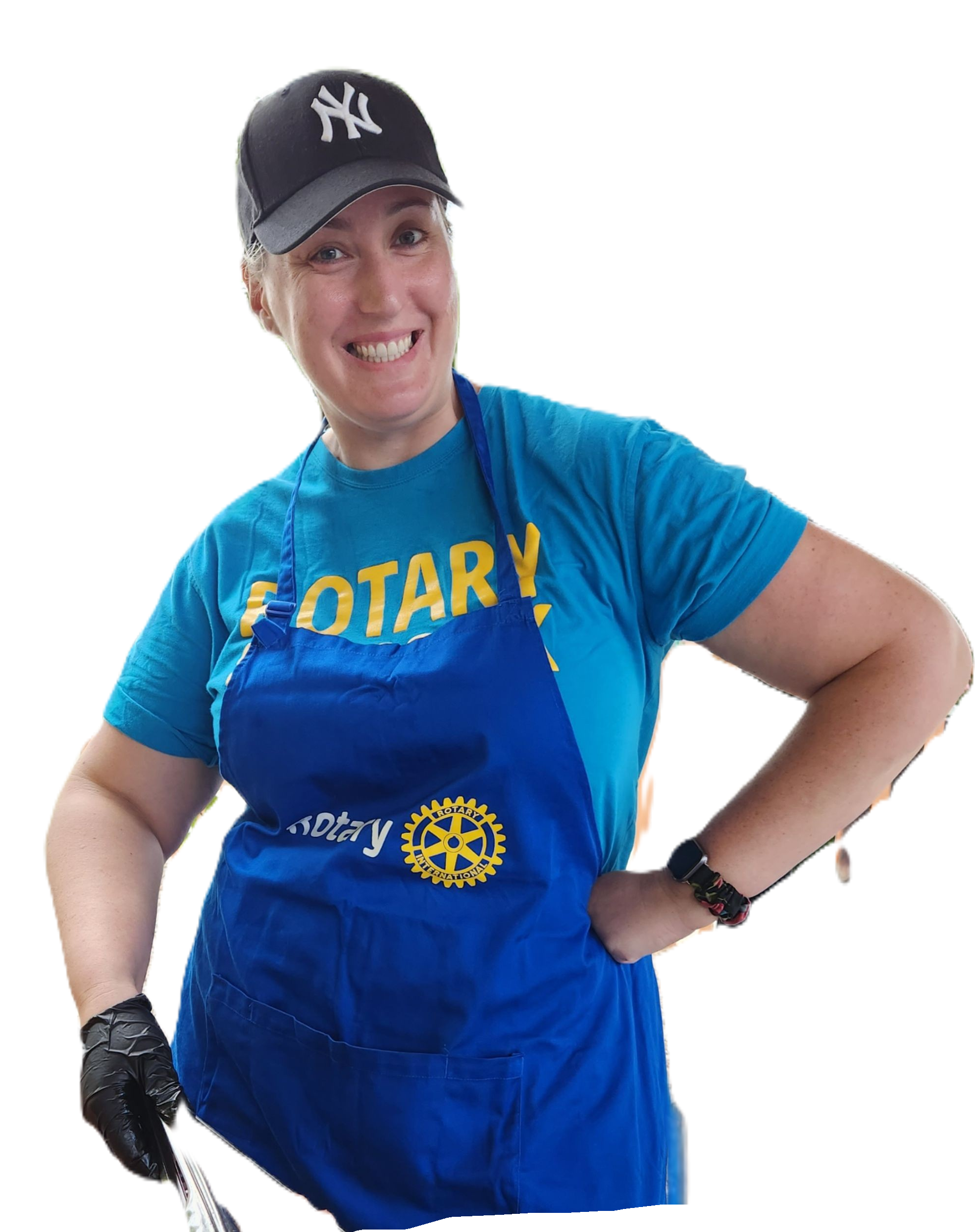 A smiling woman wearing a Yankees cap, a blue Rotary apron, and a blue Rotary t-shirt, standing with her hand on her hip, holding tongs, and wearing a black glove on one hand.