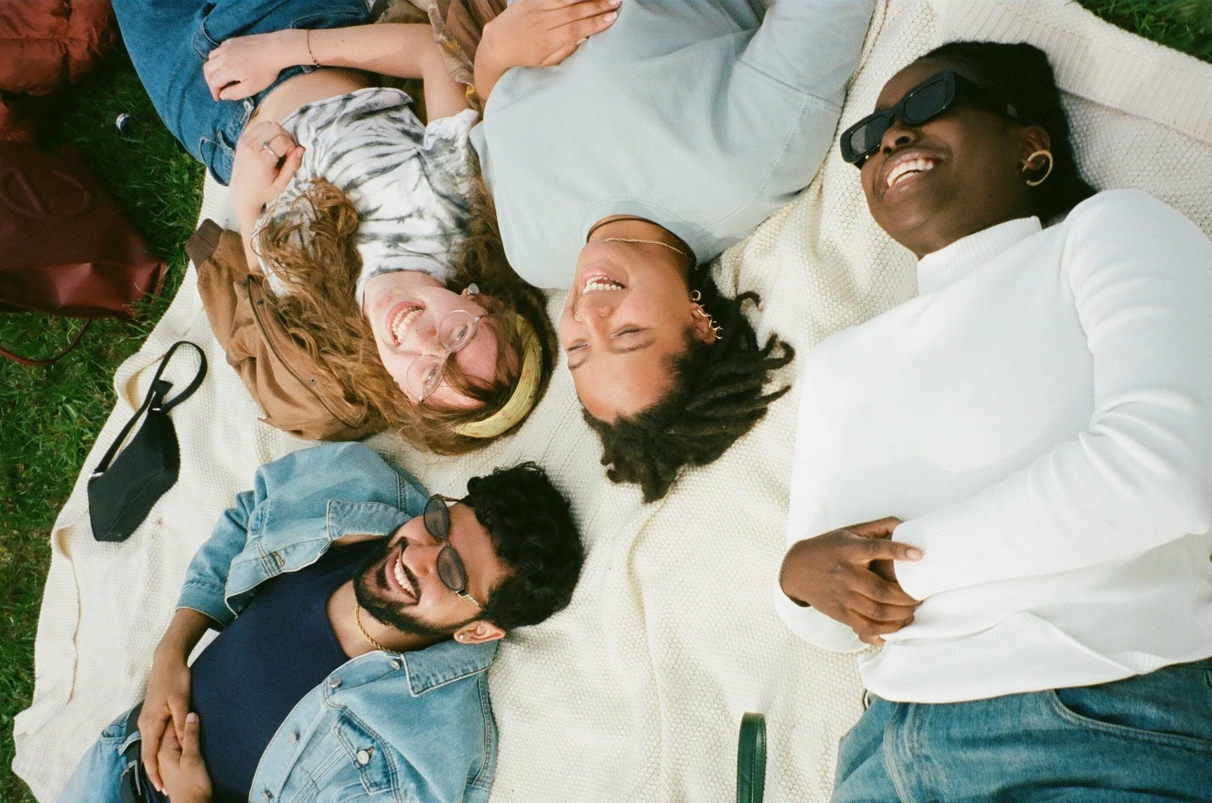 Group of five friends lying on a blanket on the grass, smiling and having fun together.