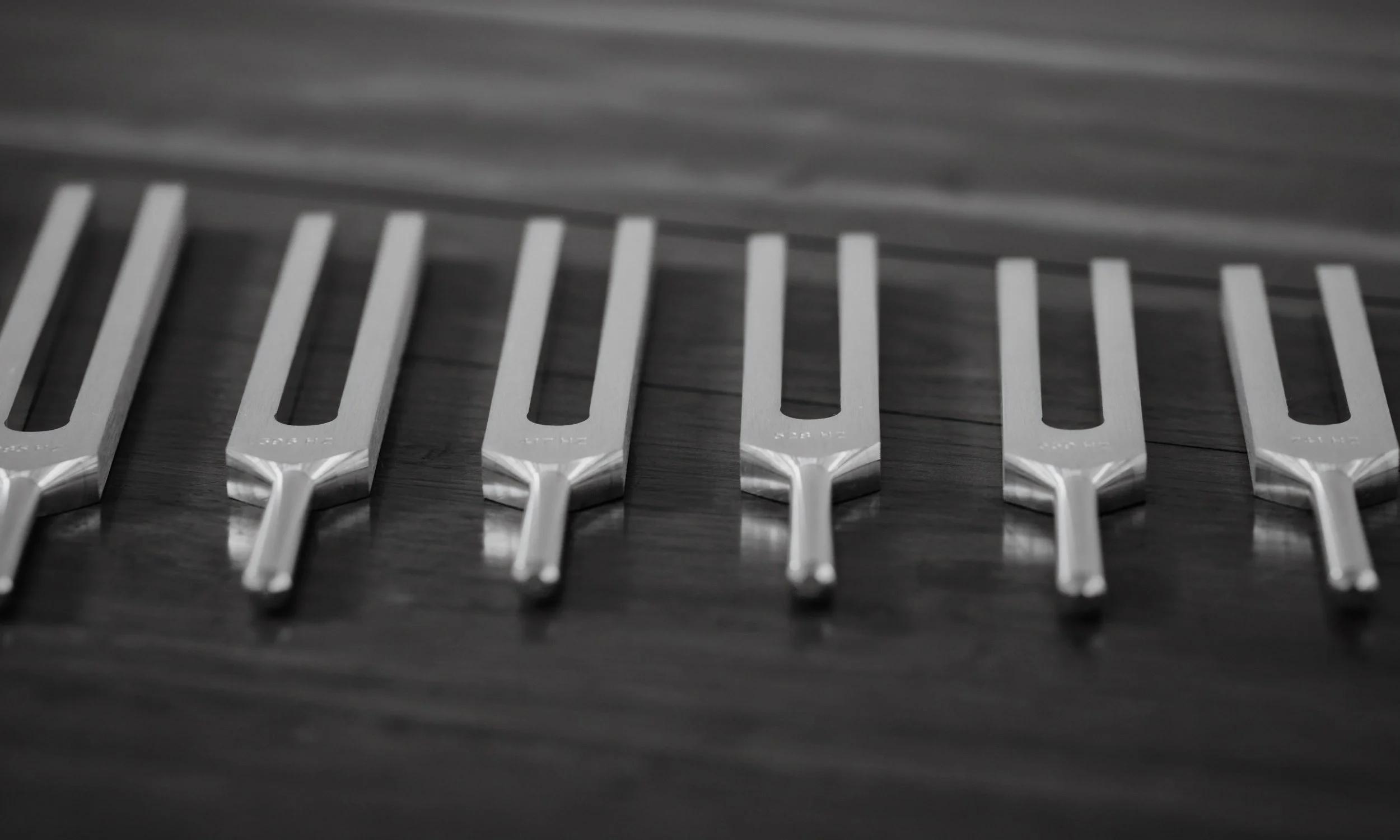 A close-up of metal tuning forks with one side on a dark surface and the other side in the air, arranged in a row.