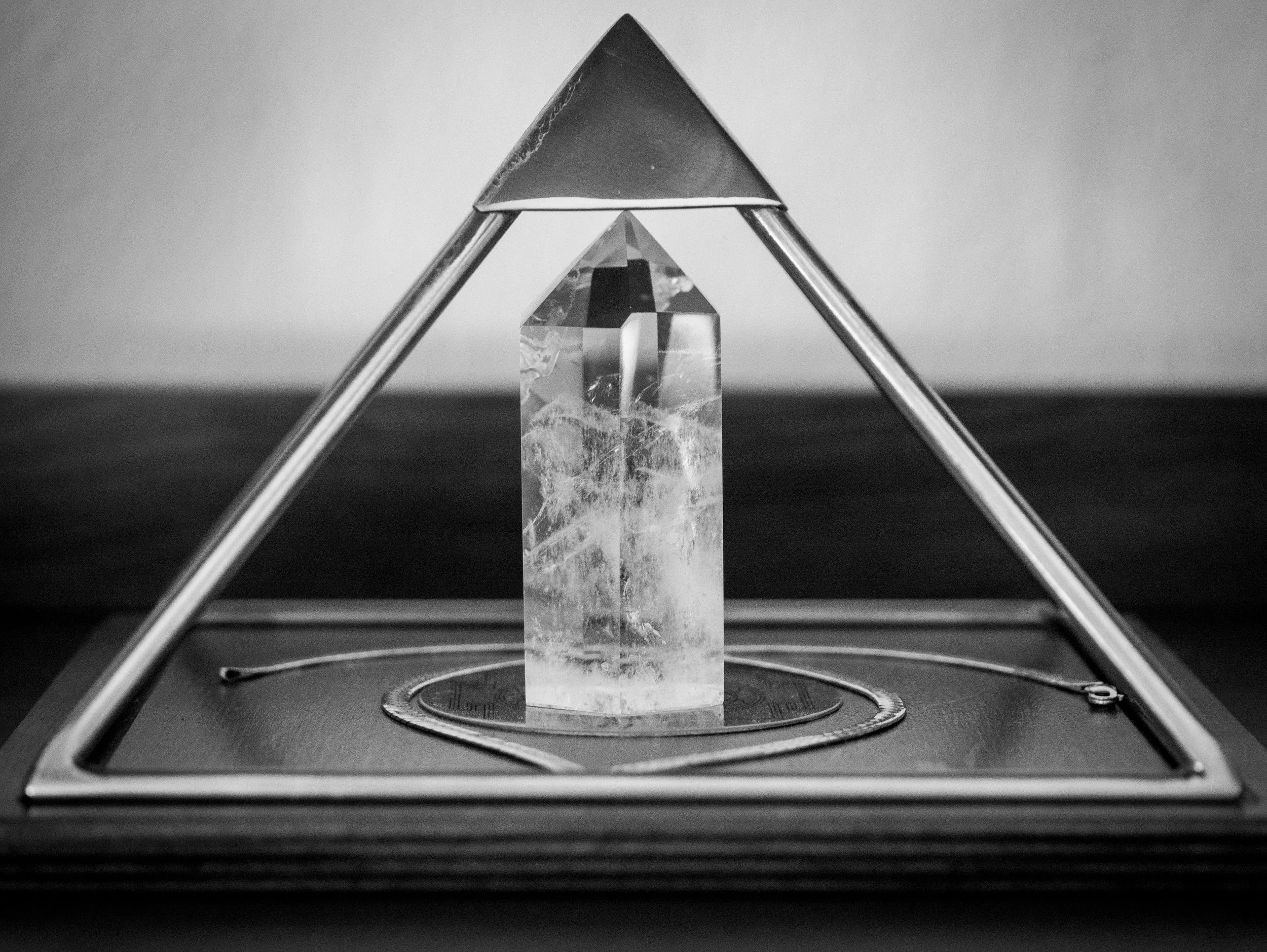 A close-up image of a geometric crystal sculpture placed on a round platform, with two metal rods supporting a triangular top piece.