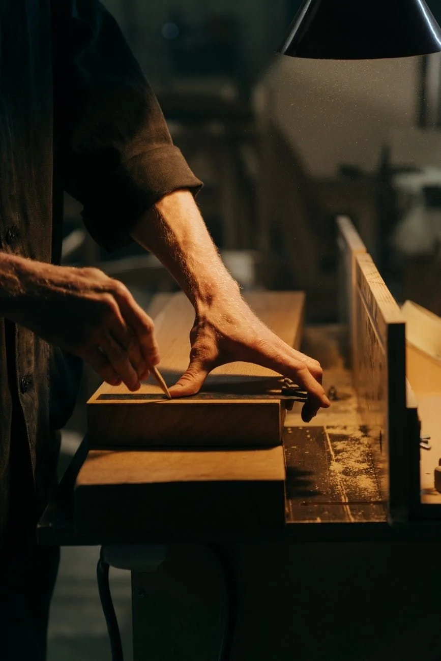 Person working on a woodworking project, sketching or measuring a piece of wood on a workbench in a workshop.