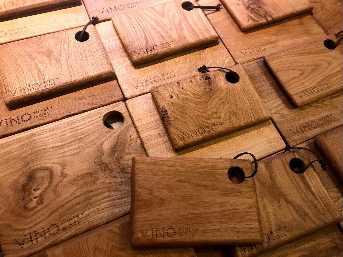 Multiple wooden wine and cheese tasting boards with engraving and black rubber ties on a wooden surface.