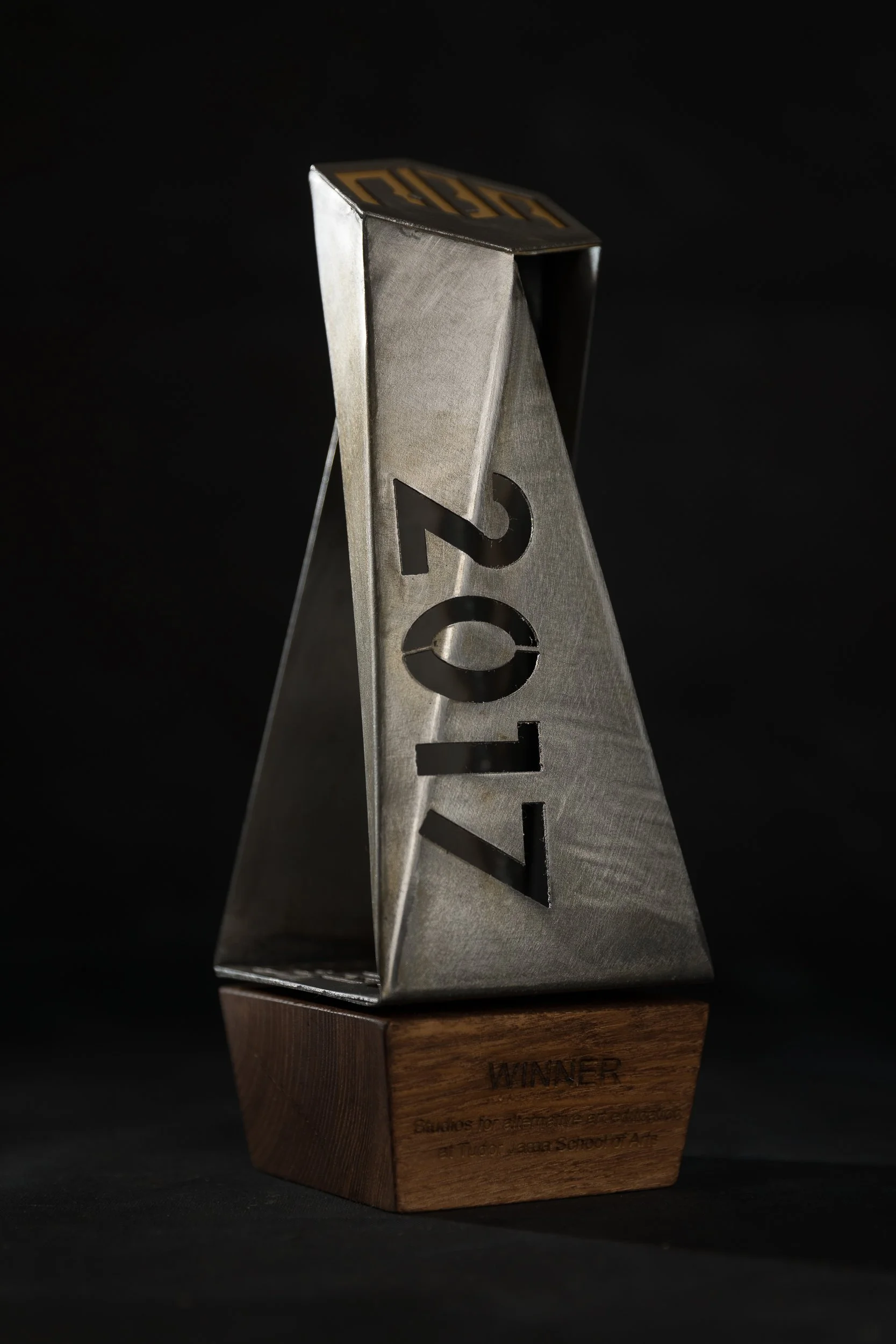 A metallic award trophy with the year 2021 cut out in the middle, mounted on a wooden base with engraved text that reads "WINNER" and additional smaller text.