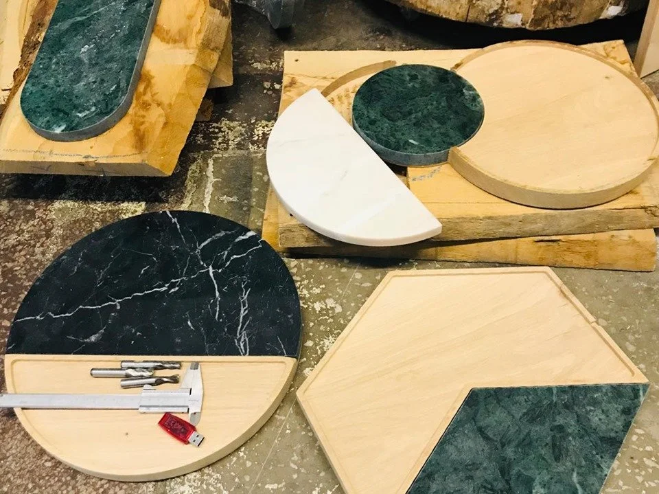 Various round and hexagonal tabletops made of marble and wood, with tools and measuring equipment on a workbench.