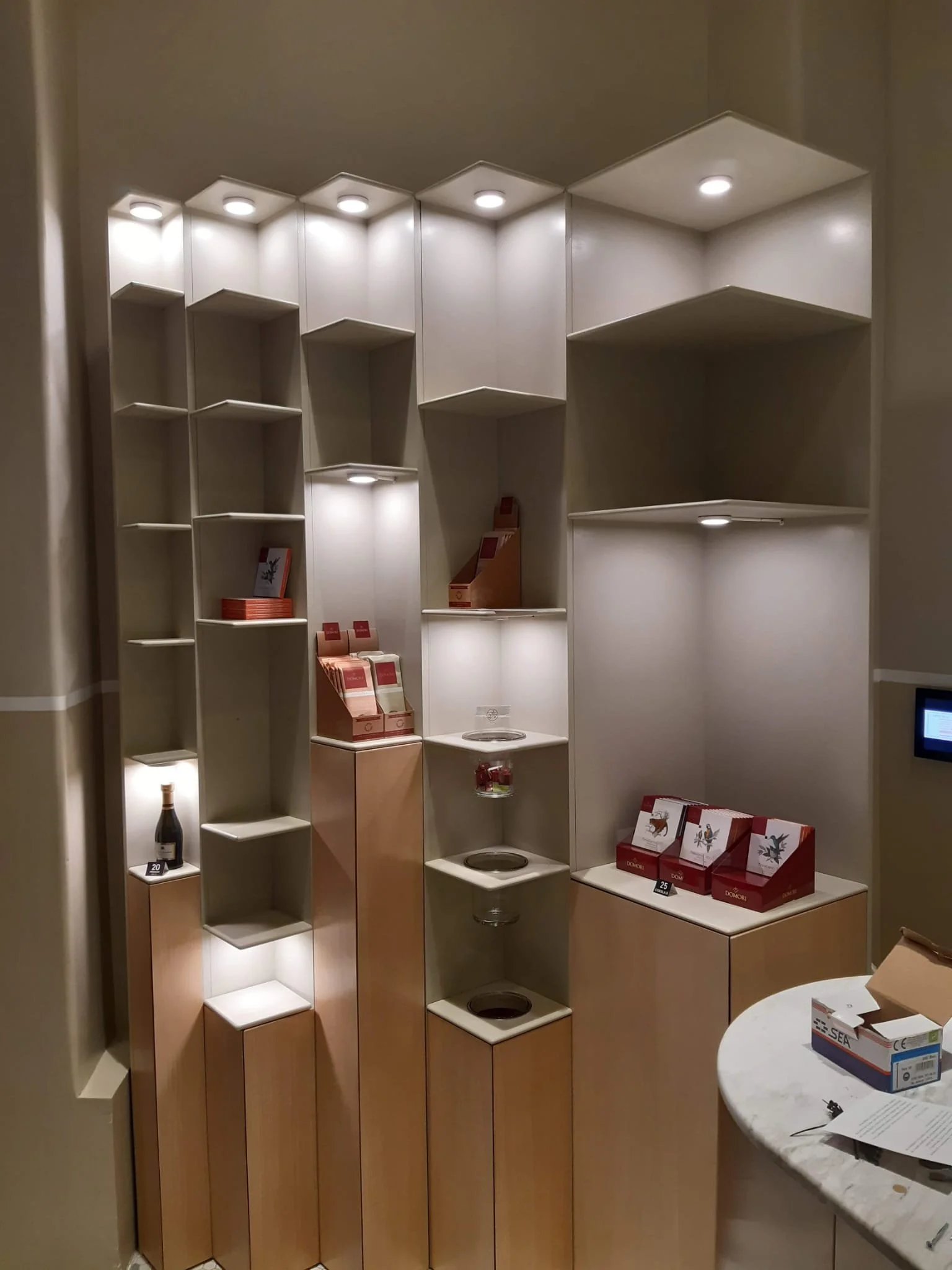 Empty retail display shelves with some boxes and items, in a modern store or shopping area, illuminated by overhead lights.