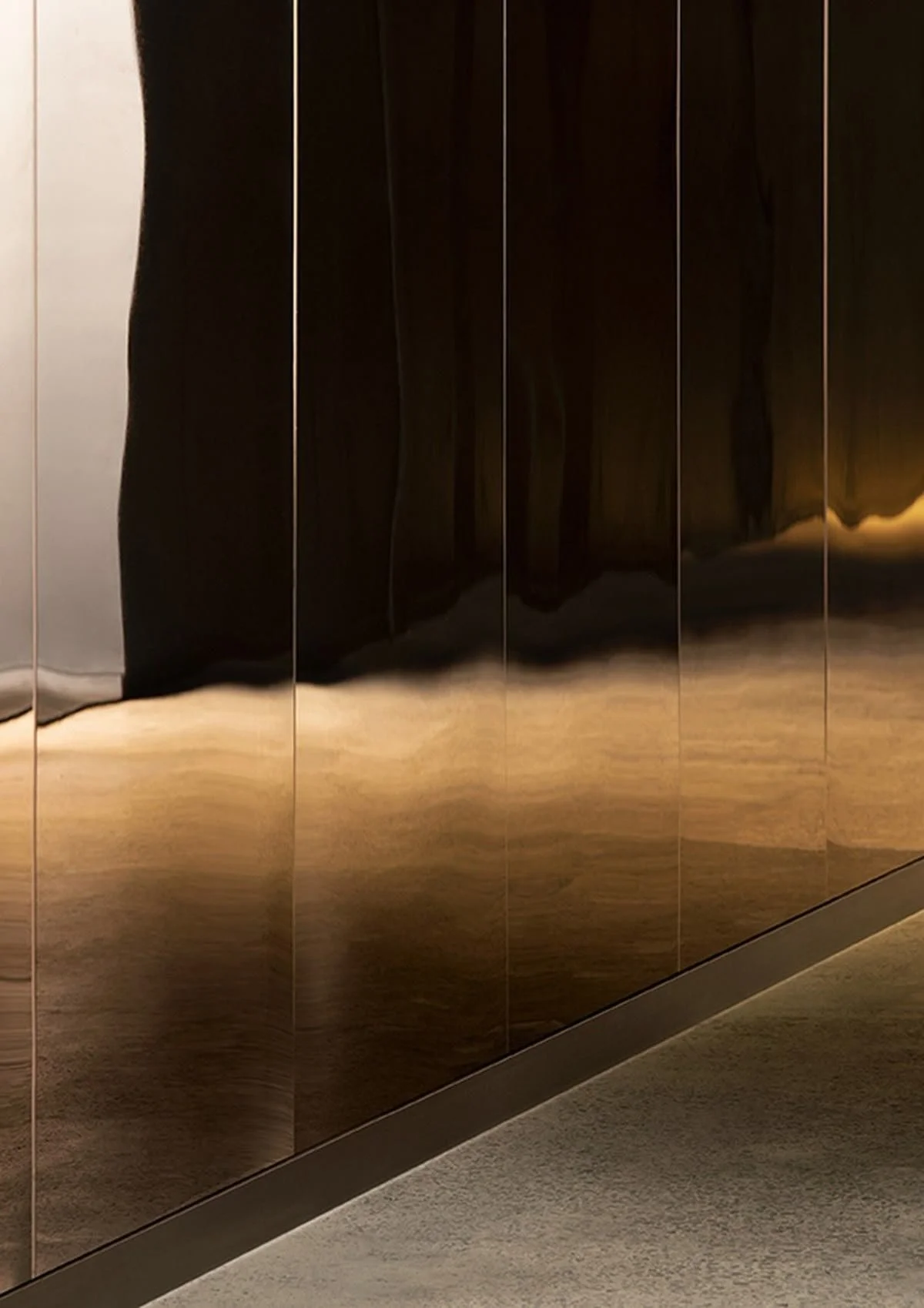 A reflective, metallic wall with vertical panels and a wooden floor. The wall's reflection creates a distorted mirror image.