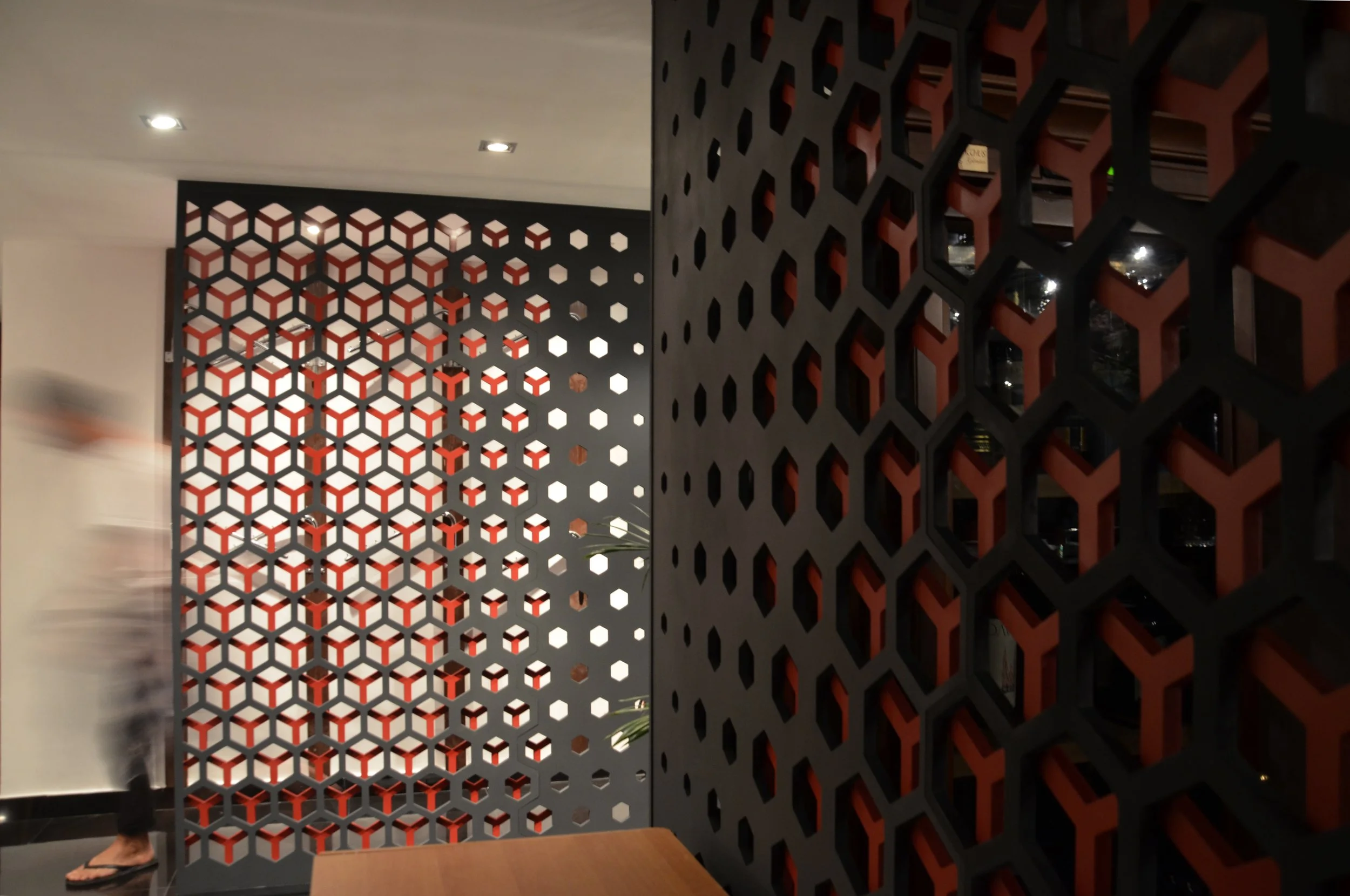 Decorative black and red hexagonal lattice room divider in a modern interior setting, with a blurred person walking past on the left.