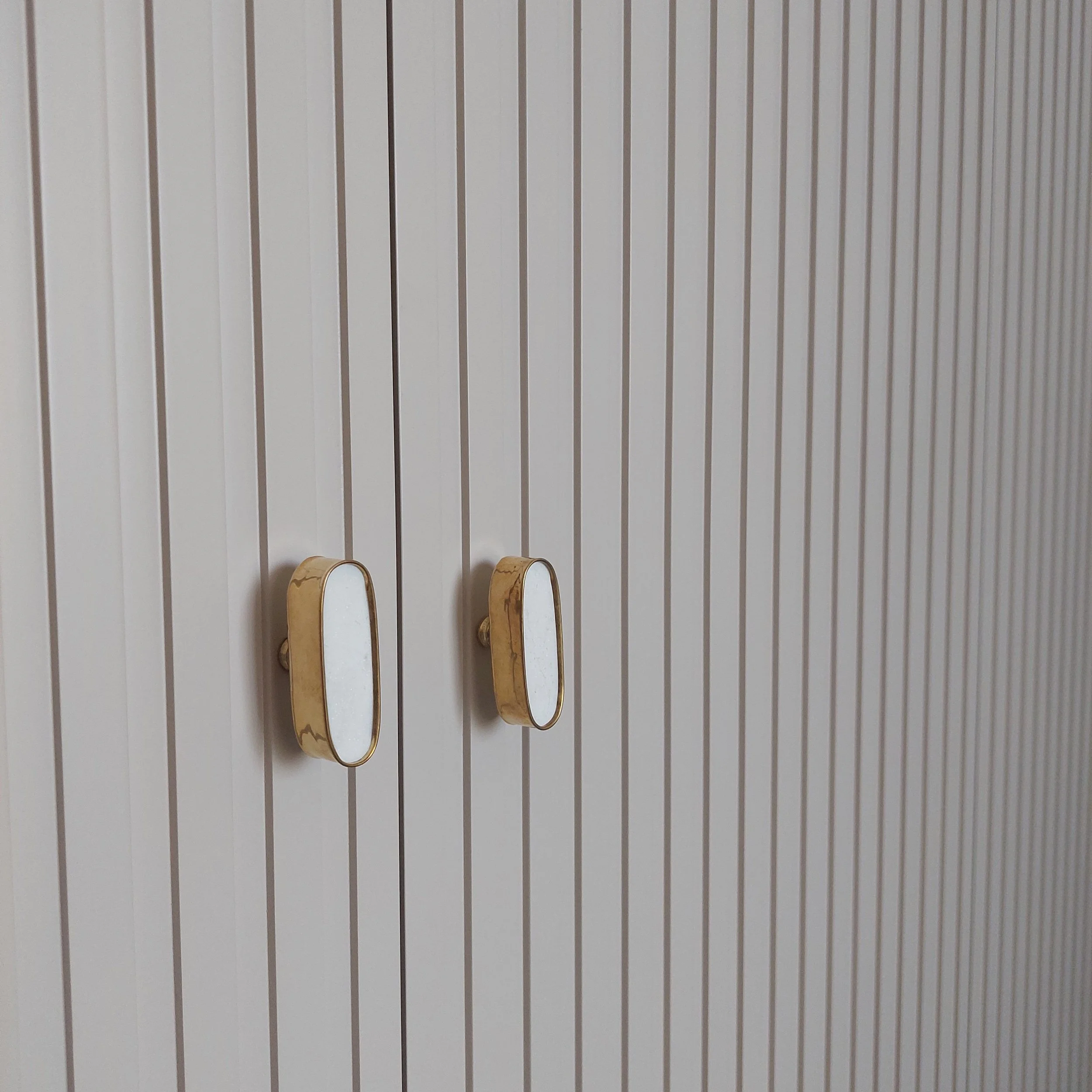A beige closet with vertical ridges and two oval-shaped gold handles.