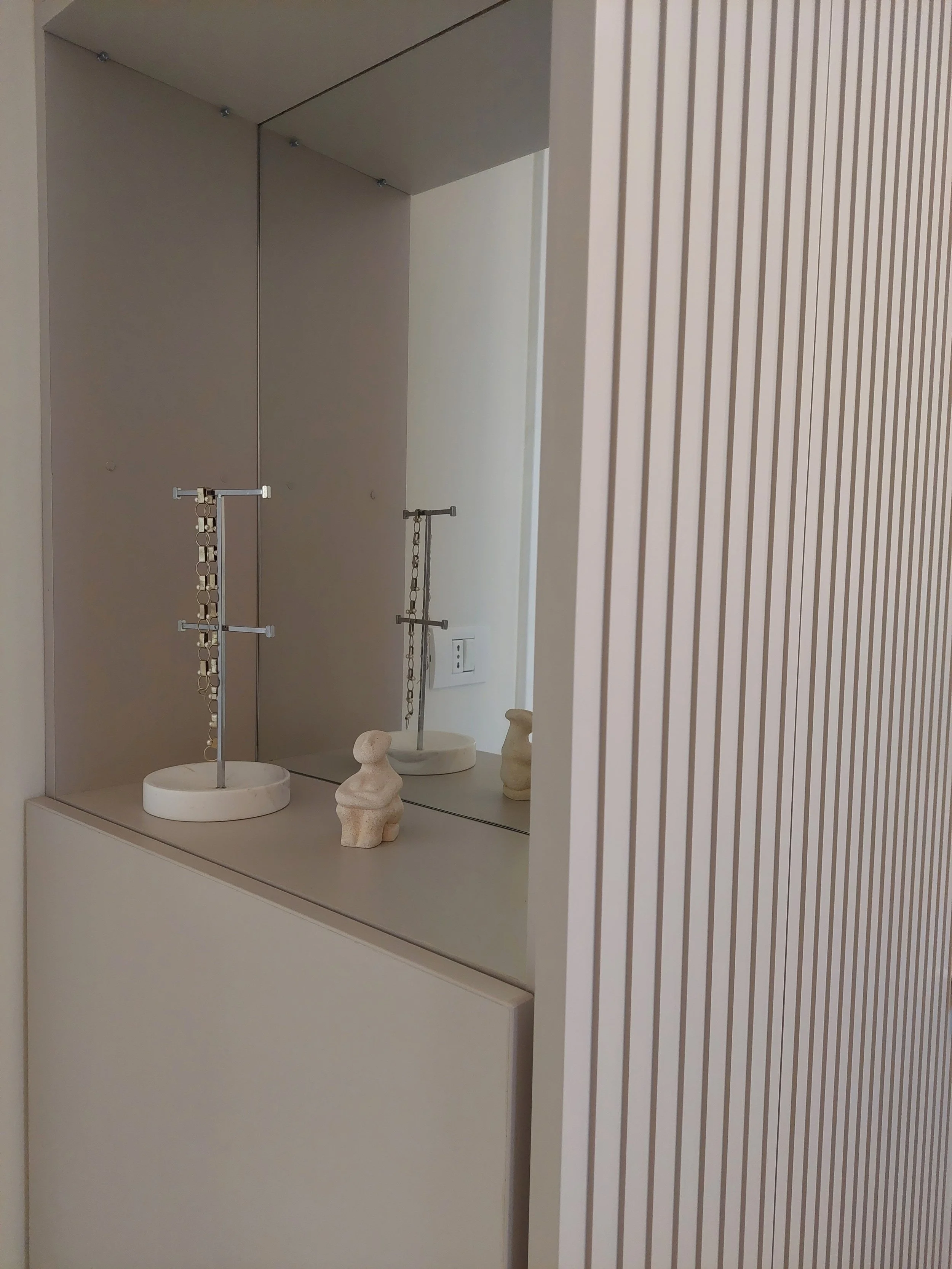 Decorative display with minimalist jewelry stands, small abstract sculptures, and a mirror reflecting part of the display, set against a neutral-toned wall in a modern interior.