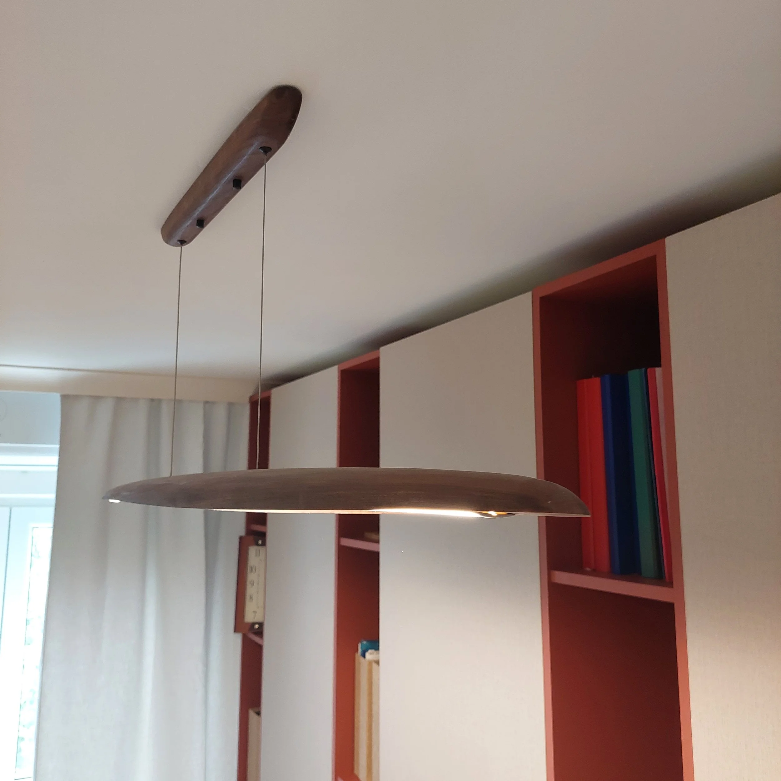A modern room ceiling with a wooden pendant light and a partial view of a bookshelf with colorful books.