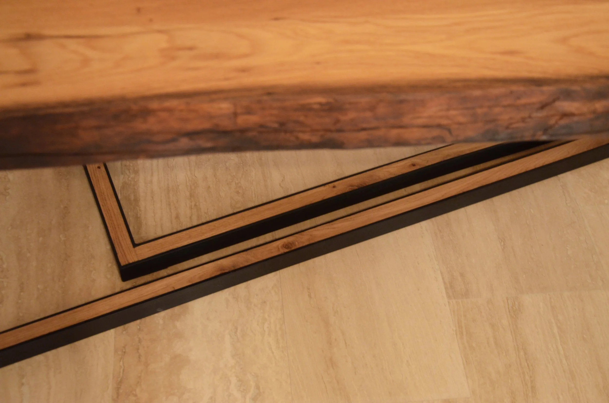 Close-up of a wooden door threshold with a rectangular wooden trim on a light-colored tiled floor.