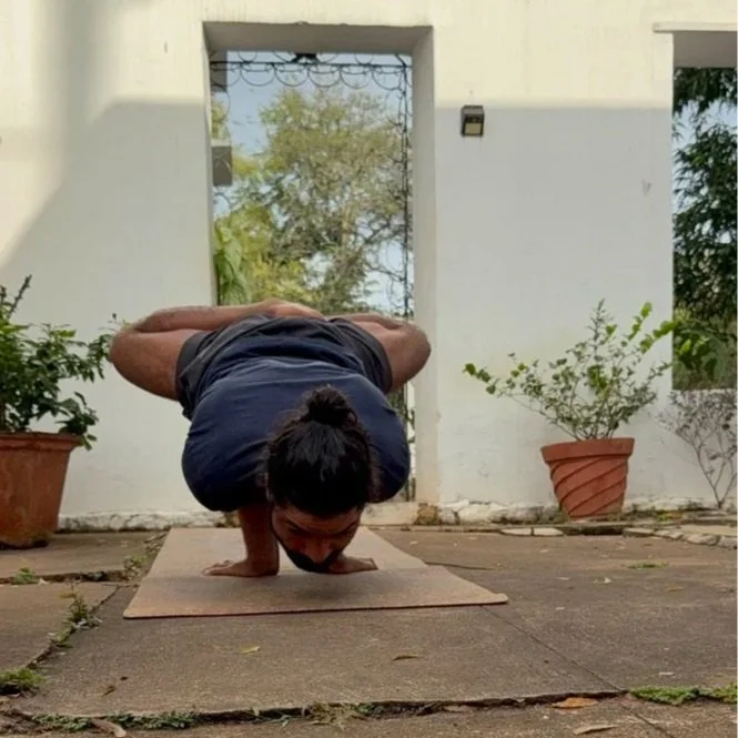 Woman practicing advanced yoga pose outside on a mat, balancing on her head with arms bent and legs stretched behind.