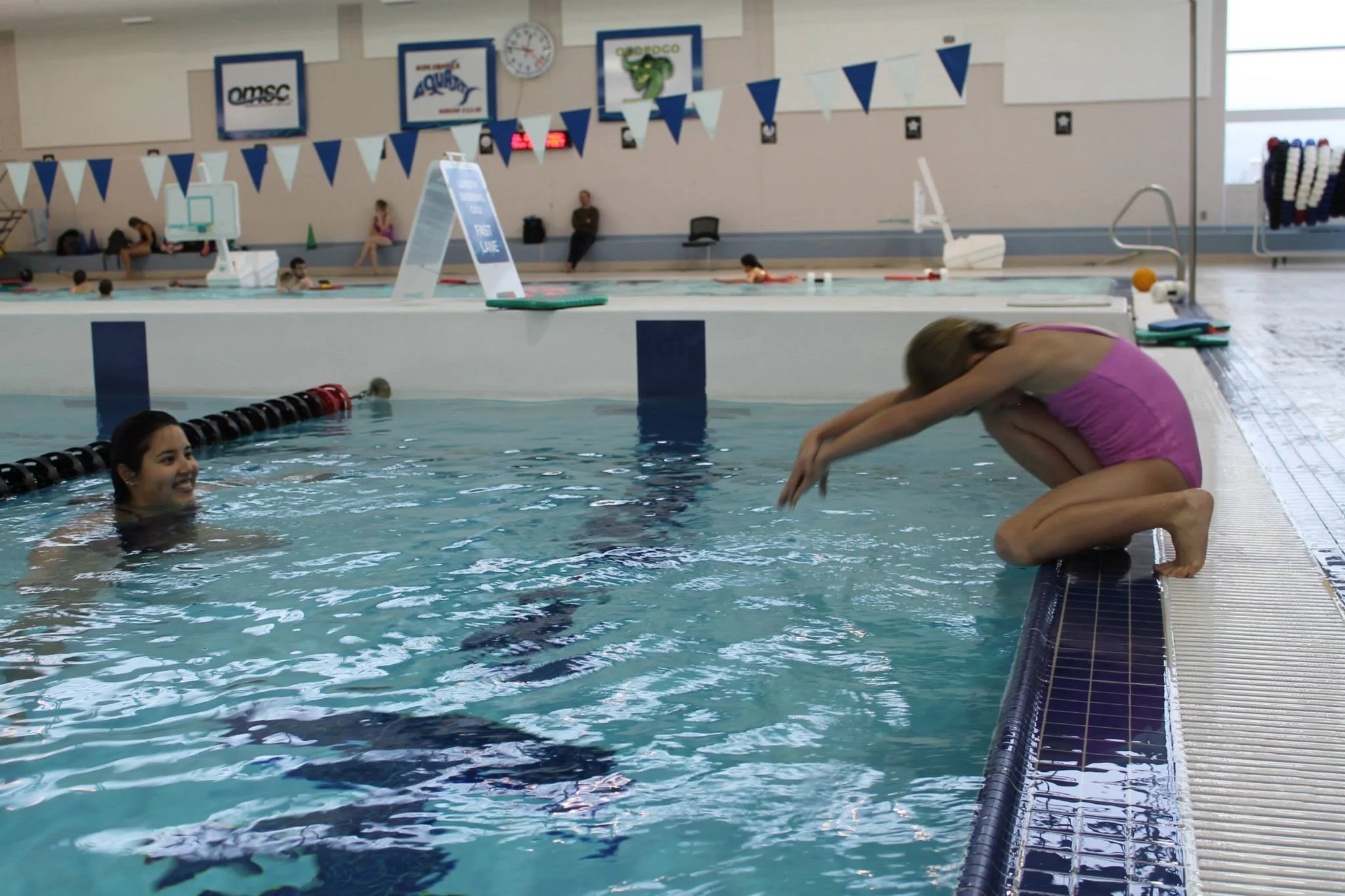 swimmer preparing to do a kneeling dive off the side of the pool, instructor watching and smiling