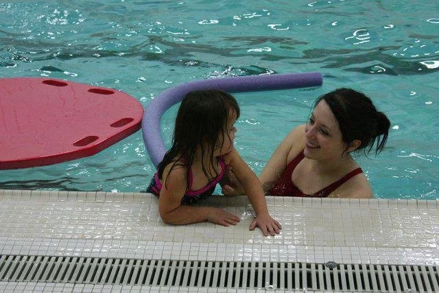 instructor smiling at swimmer who is holding on to edge of pool